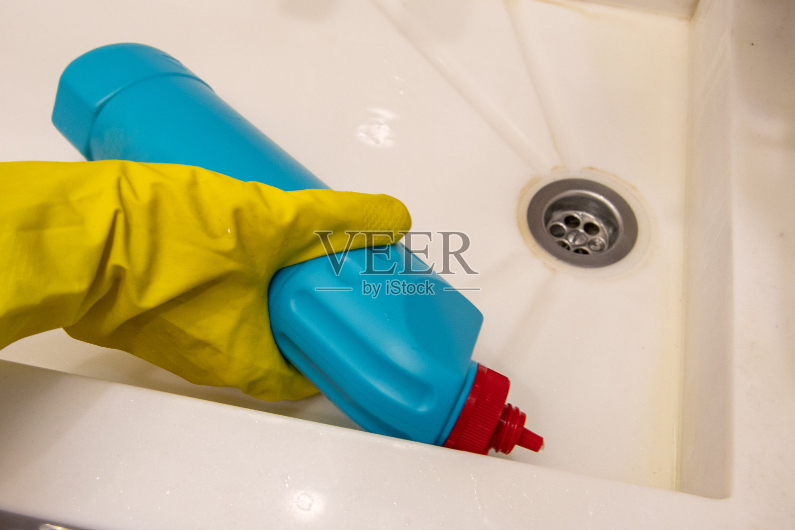 一只戴着黄色手套的手将蓝色瓶子里的清洁剂倒在水槽里。6、作业的概念，消毒照片摄影图片