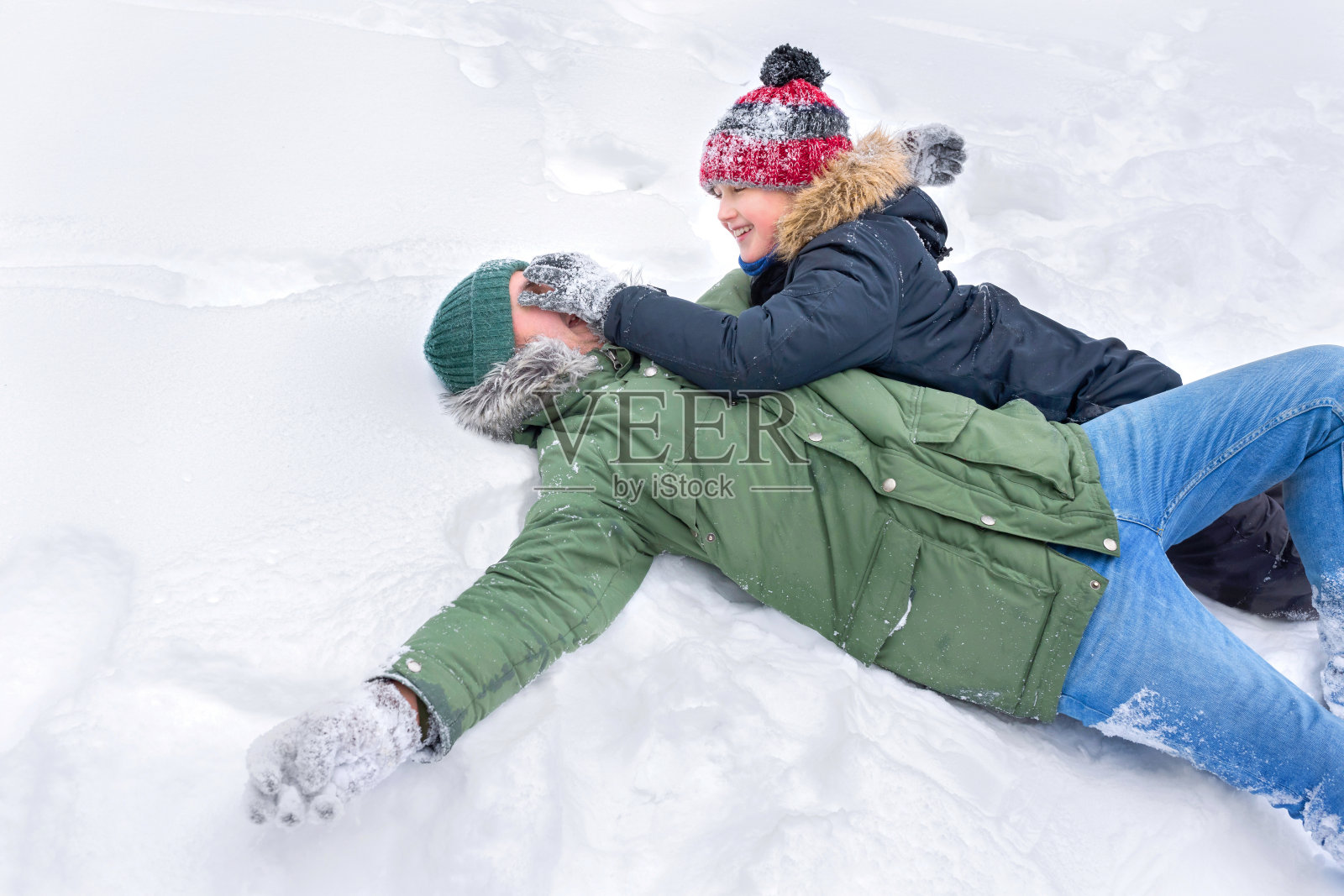 一位父亲和他10岁的儿子躺在雪地里玩雪。照片摄影图片