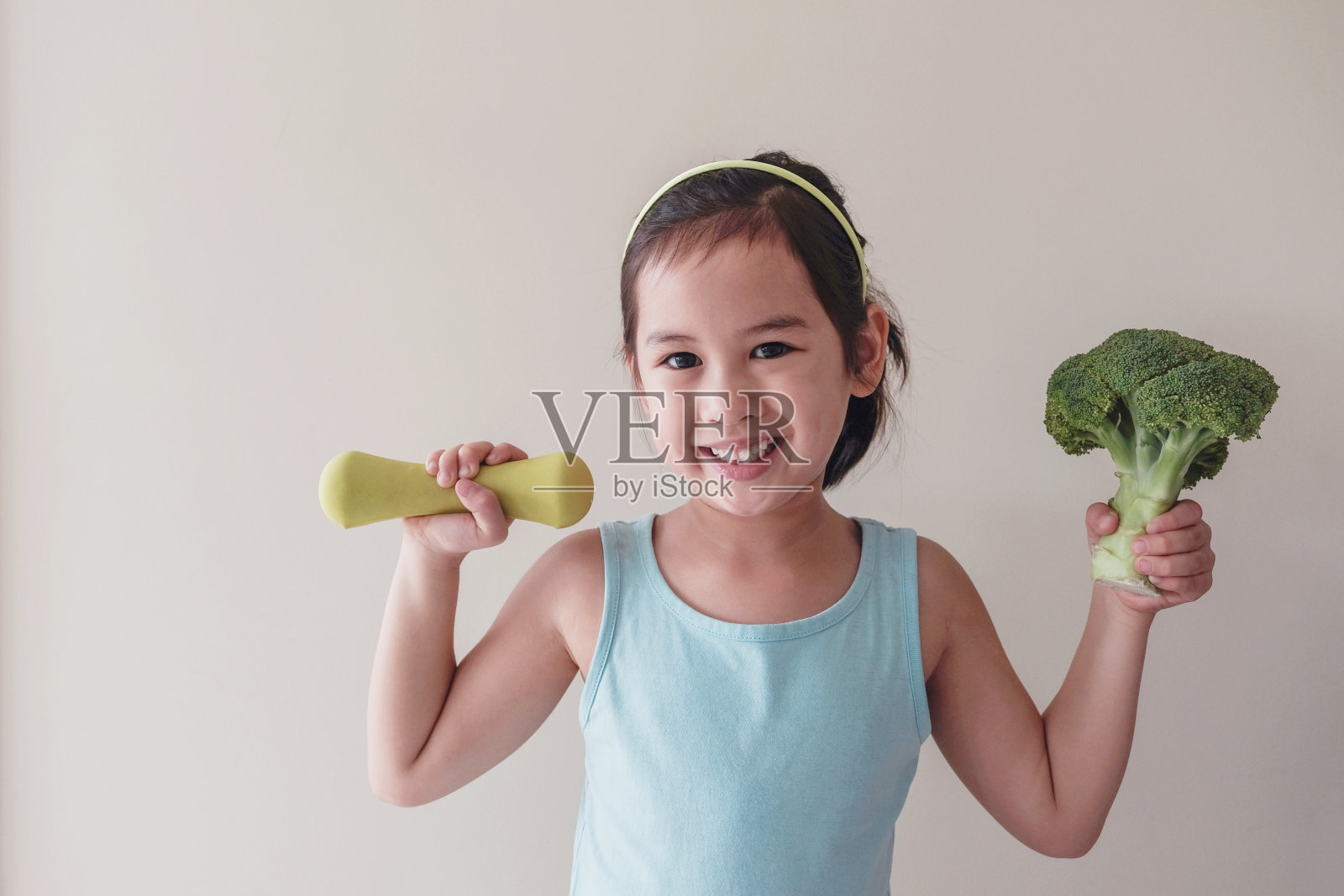 快乐和健康的混合亚洲女孩举起花椰菜和哑铃，儿童健康概念照片摄影图片