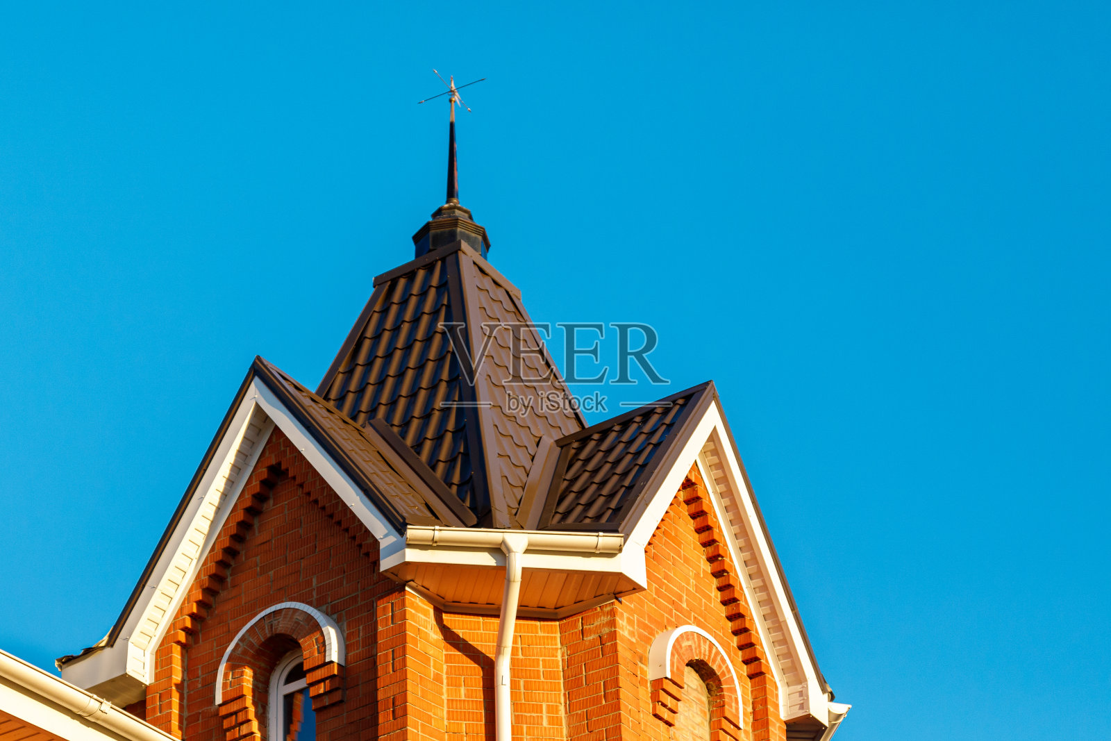 屋顶上有一座小塔。在蓝天的映衬下，一幢砖砌小屋的新金属屋顶和排水系统。照片摄影图片