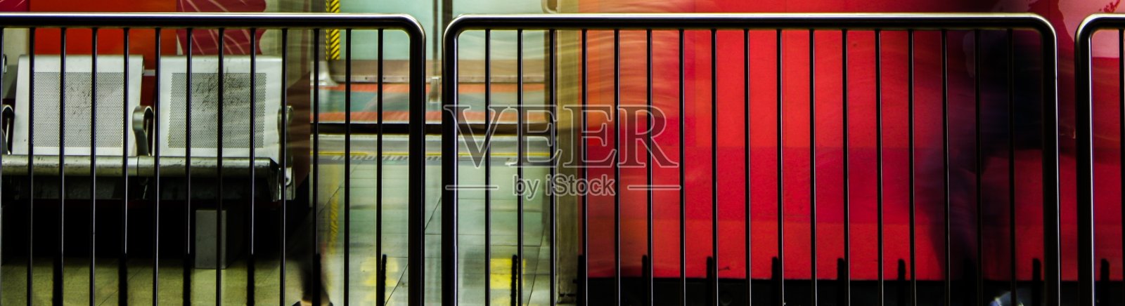 地铁站里的镀锌钢路障和空的金属椅子，模糊的通勤者在红墙旁行走照片摄影图片