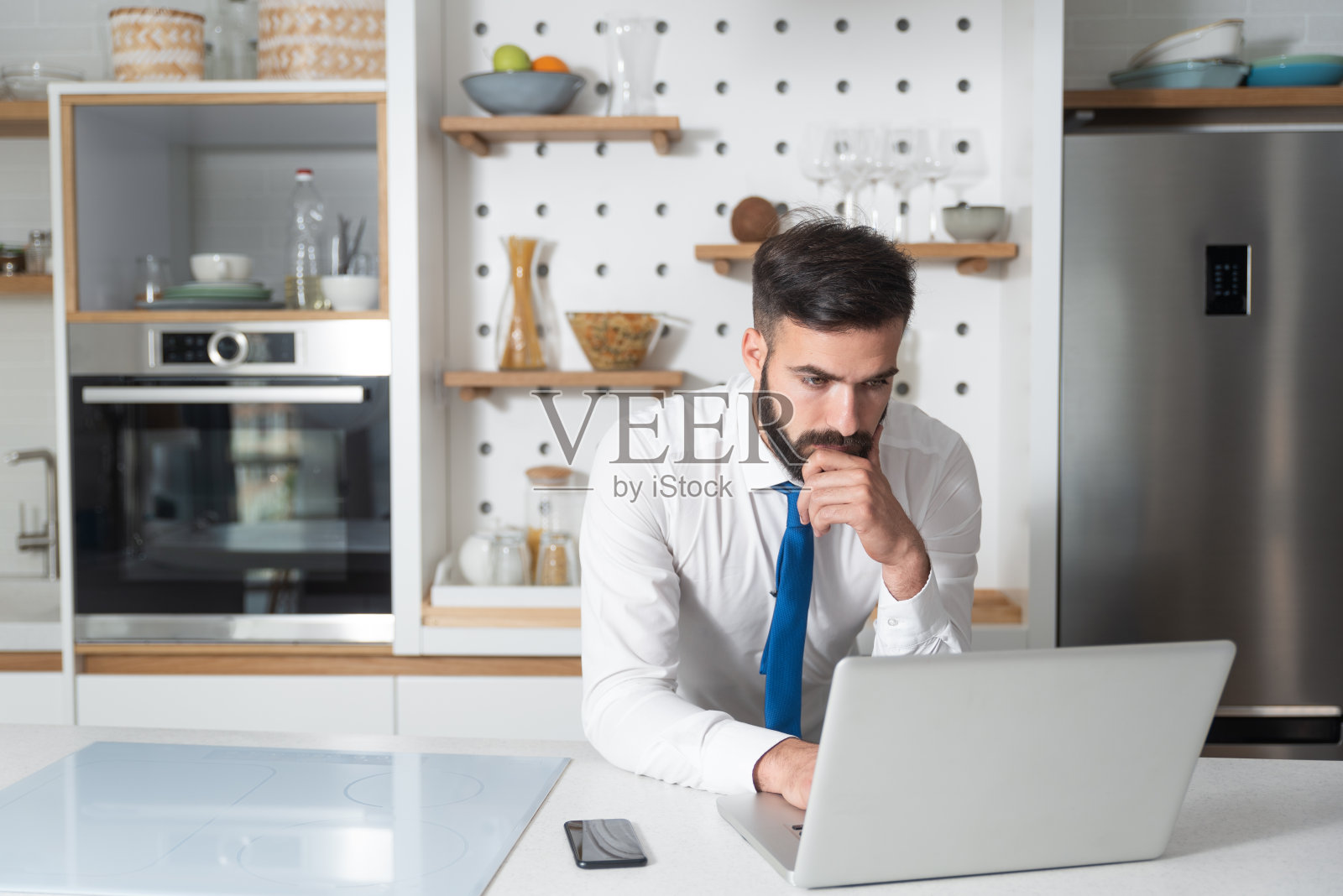 年轻的大胡子商人站在厨房里，在笔记本电脑上查看公司的工作清单，为他的新商业计划和项目做准备照片摄影图片