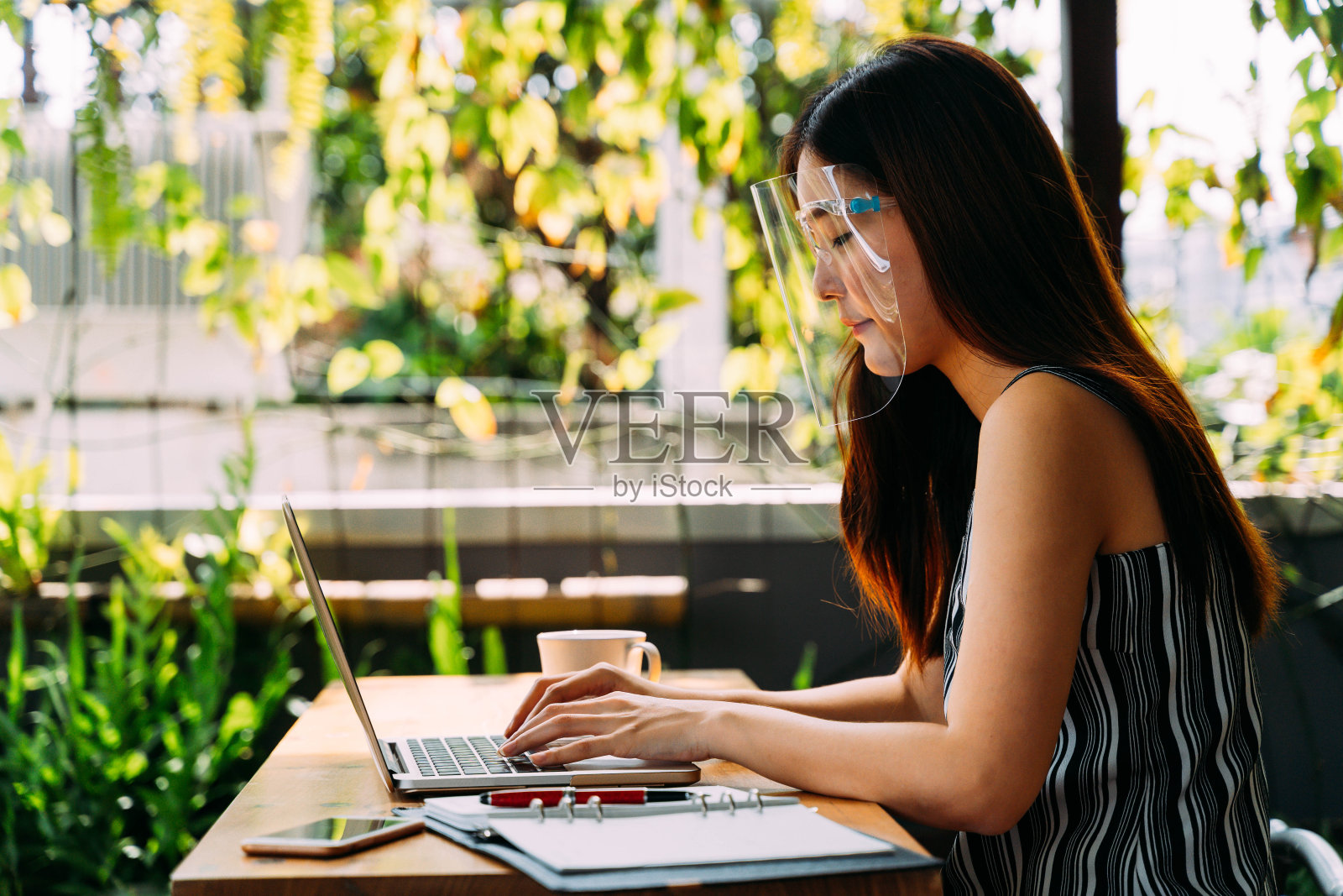 亚洲妇女戴着面罩，坐在外面用笔记本电脑工作。在户外办公室使用电脑。面罩是流行的设备，以防止冠状病毒在亚洲照片摄影图片