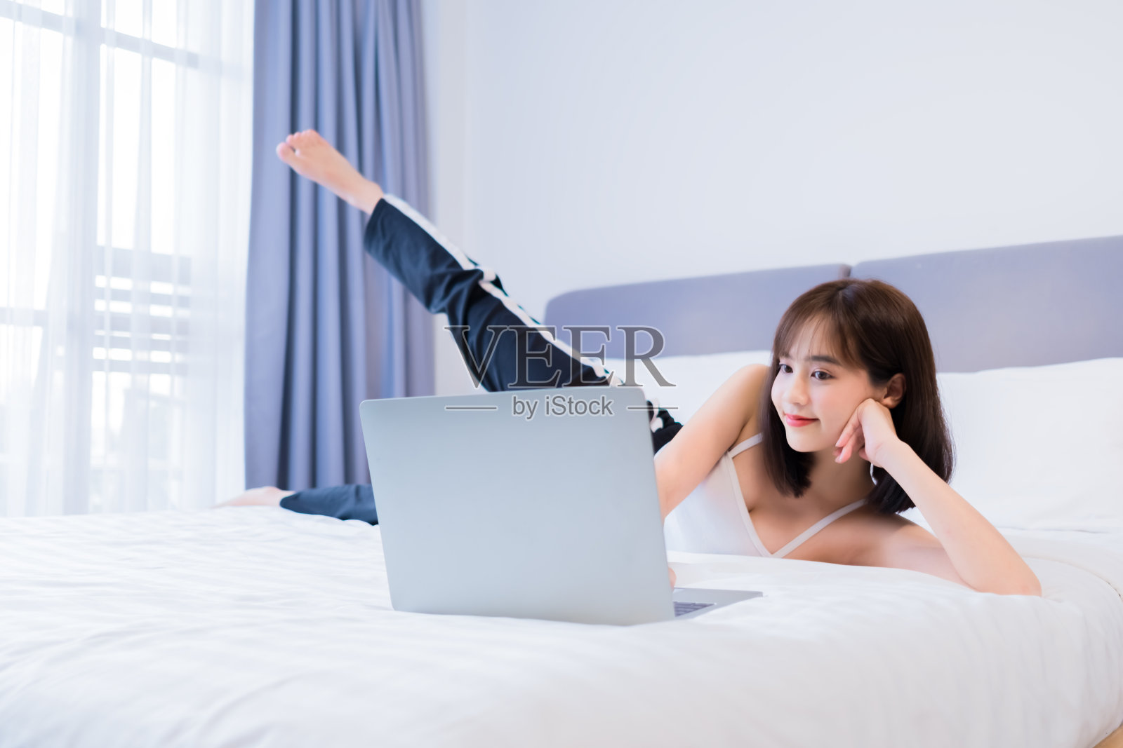 年轻的亚洲妇女在床上伸展运动，在家里的笔记本电脑上看在线教程。照片摄影图片