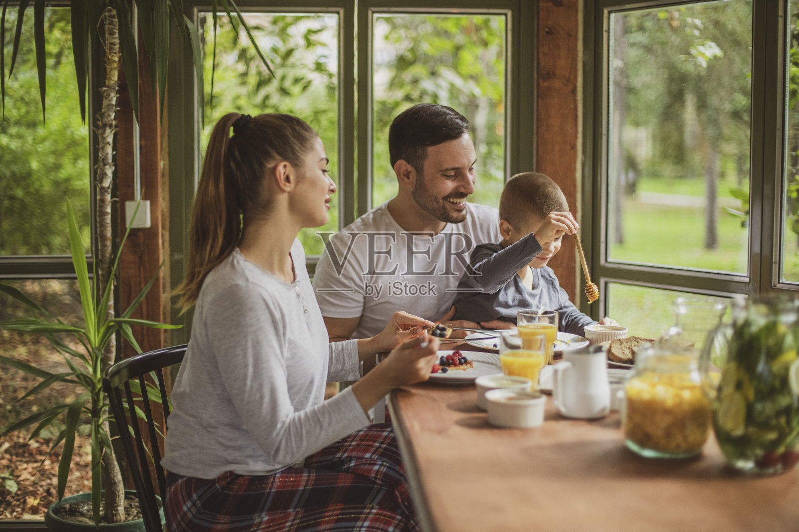 一个年轻的家庭穿着睡衣在树林里一个舒适的小木屋里吃健康的早餐。照片摄影图片