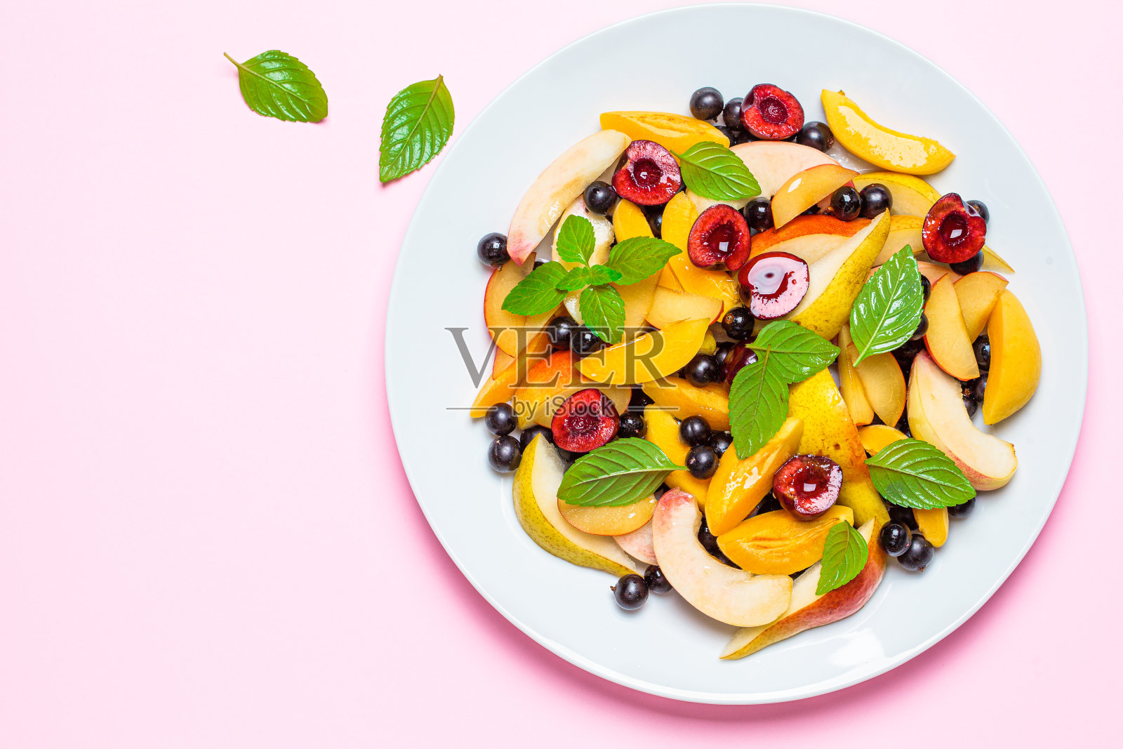 水果沙拉与浆果在白色的盘子，粉红色的背景，俯视图。健康素食的概念。照片摄影图片