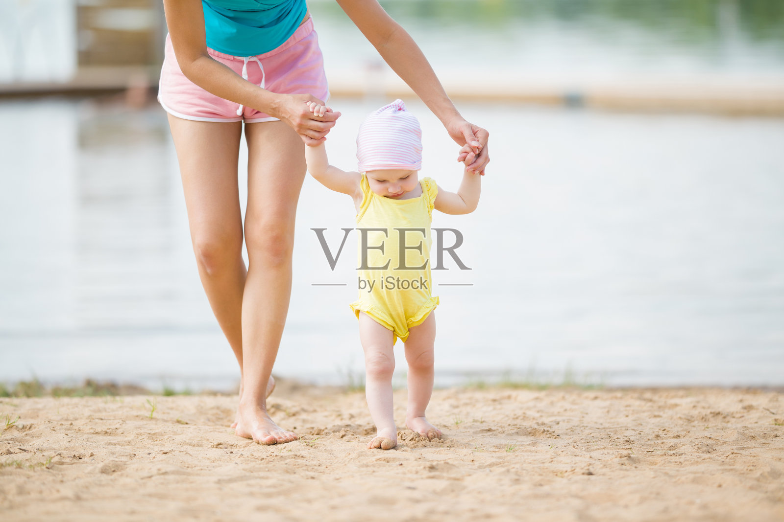 年轻的母亲帮助小女孩在海滩上迈出第一步。可爱的，和平的漫步在夏日的沙滩上。前视图。照片摄影图片