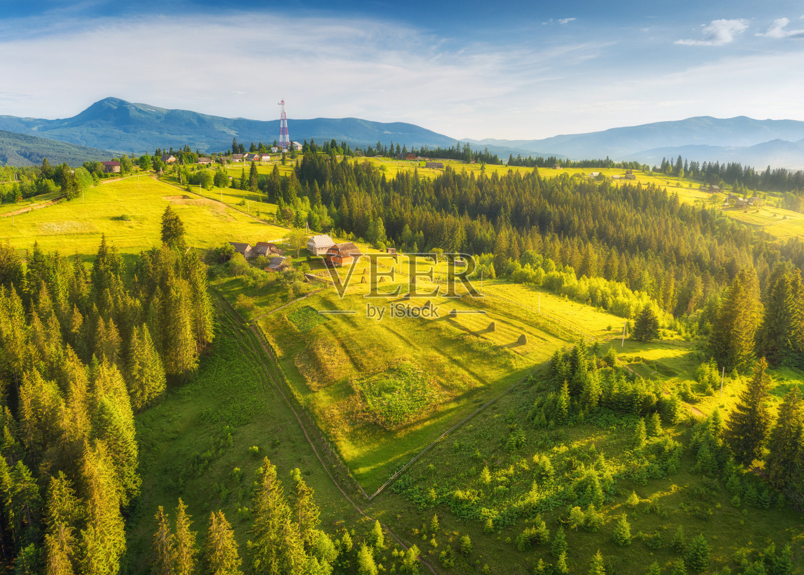 鸟瞰图美丽的小村庄在喀尔巴阡山脉在夏季日落。五颜六色的风景与绿色的草地，房屋与花园，松树，多云的天空。俯视图的山区乡村照片摄影图片