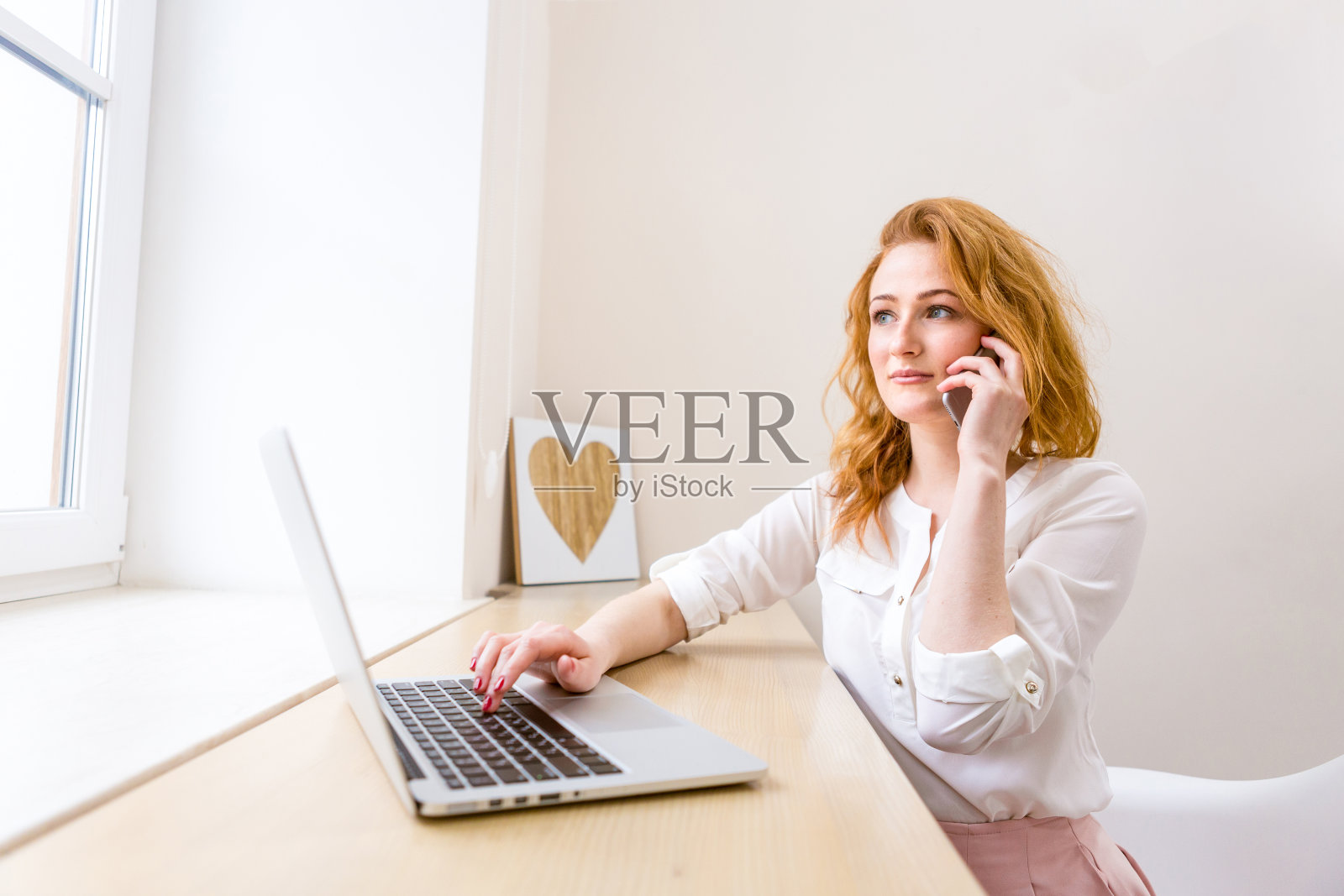 肖像职业女性工作在书桌上笔记本电脑和智能手机，微笑电话交谈，办公室内部。工作的女性的生活方式。女商人打电话照片摄影图片