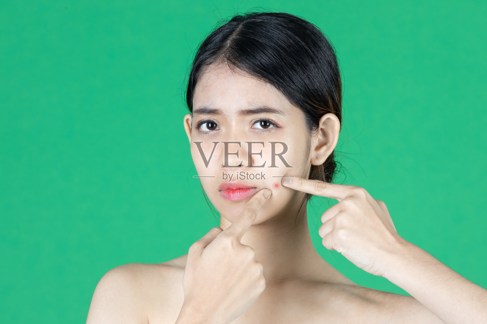 担心焦虑的年轻亚洲妇女触摸她的皮肤用手指和看痤疮问题在绿色孤立的背景。美容护肤理念。照片摄影图片