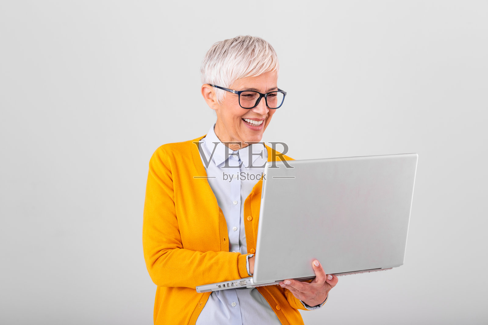 一个开朗成熟的女人孤立地站在灰色背景下使用笔记本电脑的画面。一个微笑的高级女士的肖像拿着笔记本电脑照片摄影图片
