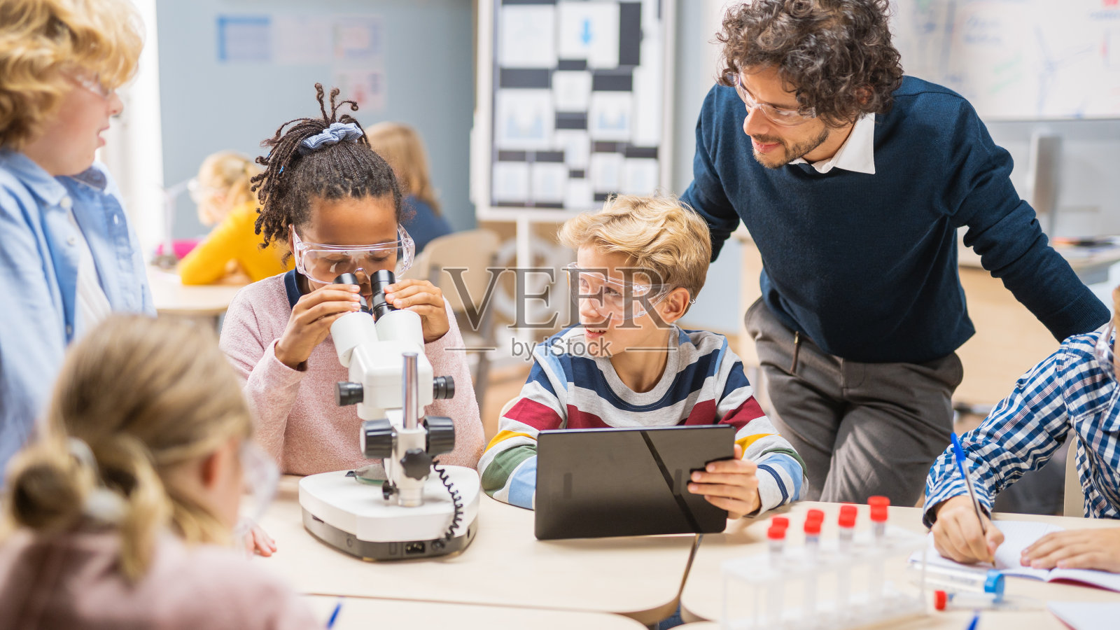 小学科学课堂:可爱的小女孩在显微镜下看，男孩在用平板电脑上网查信息，热情的老师在讲解照片摄影图片
