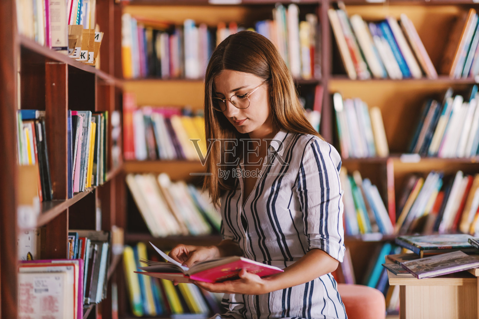年轻漂亮的女大学生站在图书馆看书。照片摄影图片