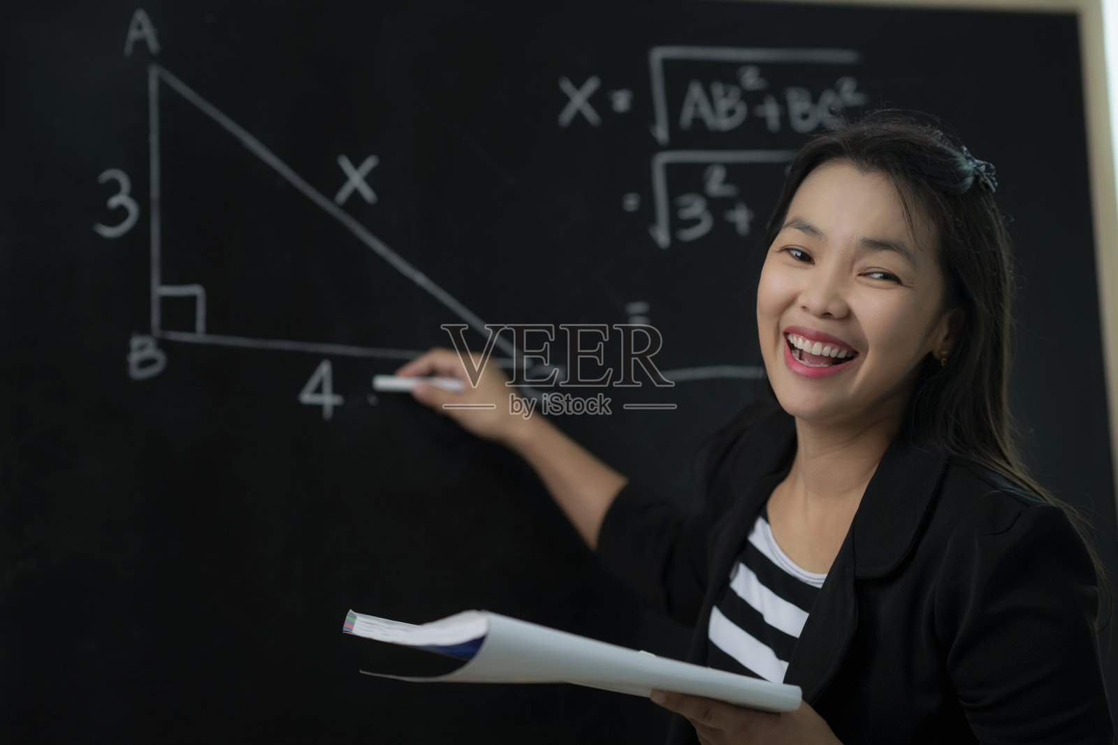 一位亚洲老师在教室里向她的学生解释数学公式照片摄影图片