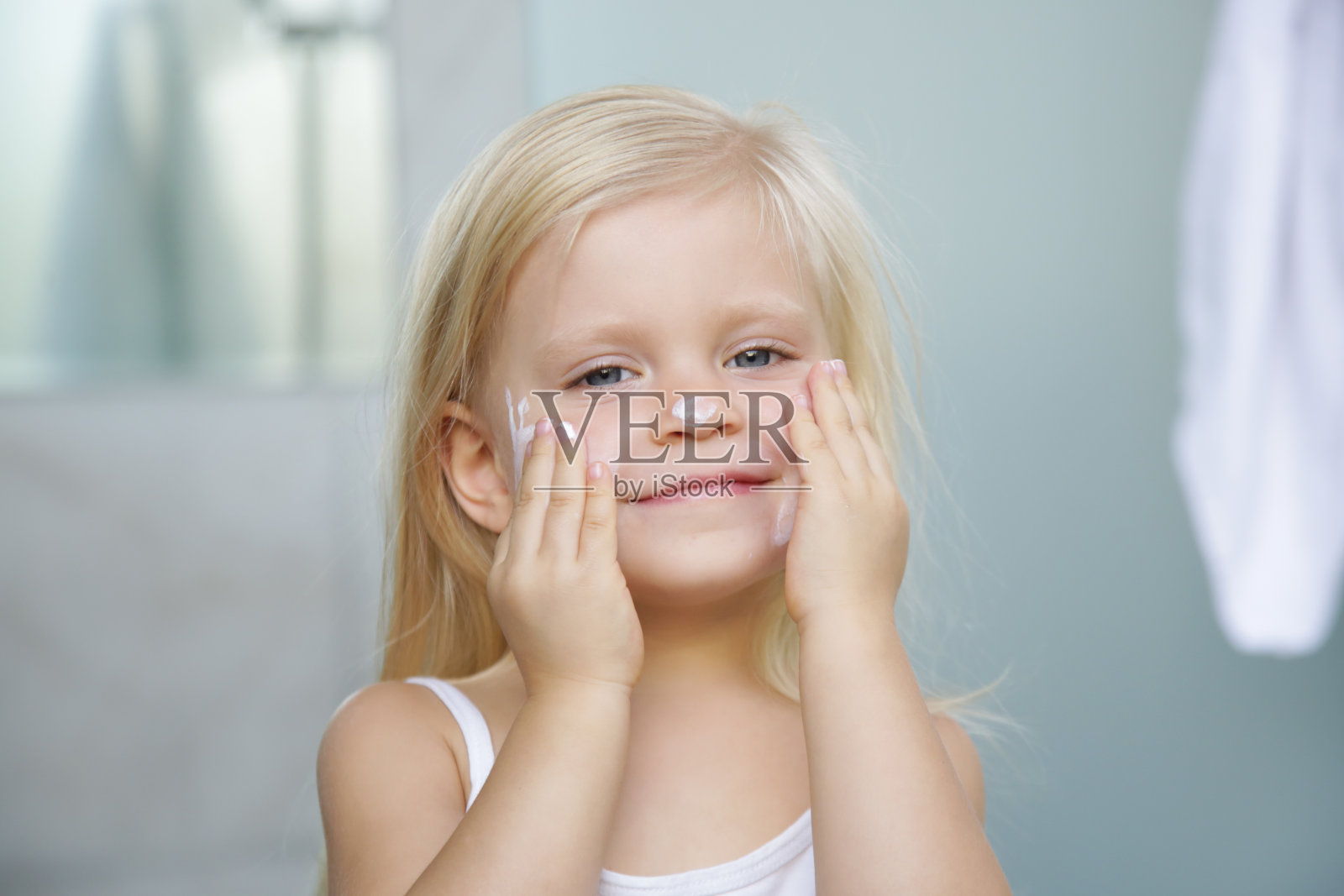 可爱的金发白种人幼童女孩在她的脸上涂抹霜照片摄影图片