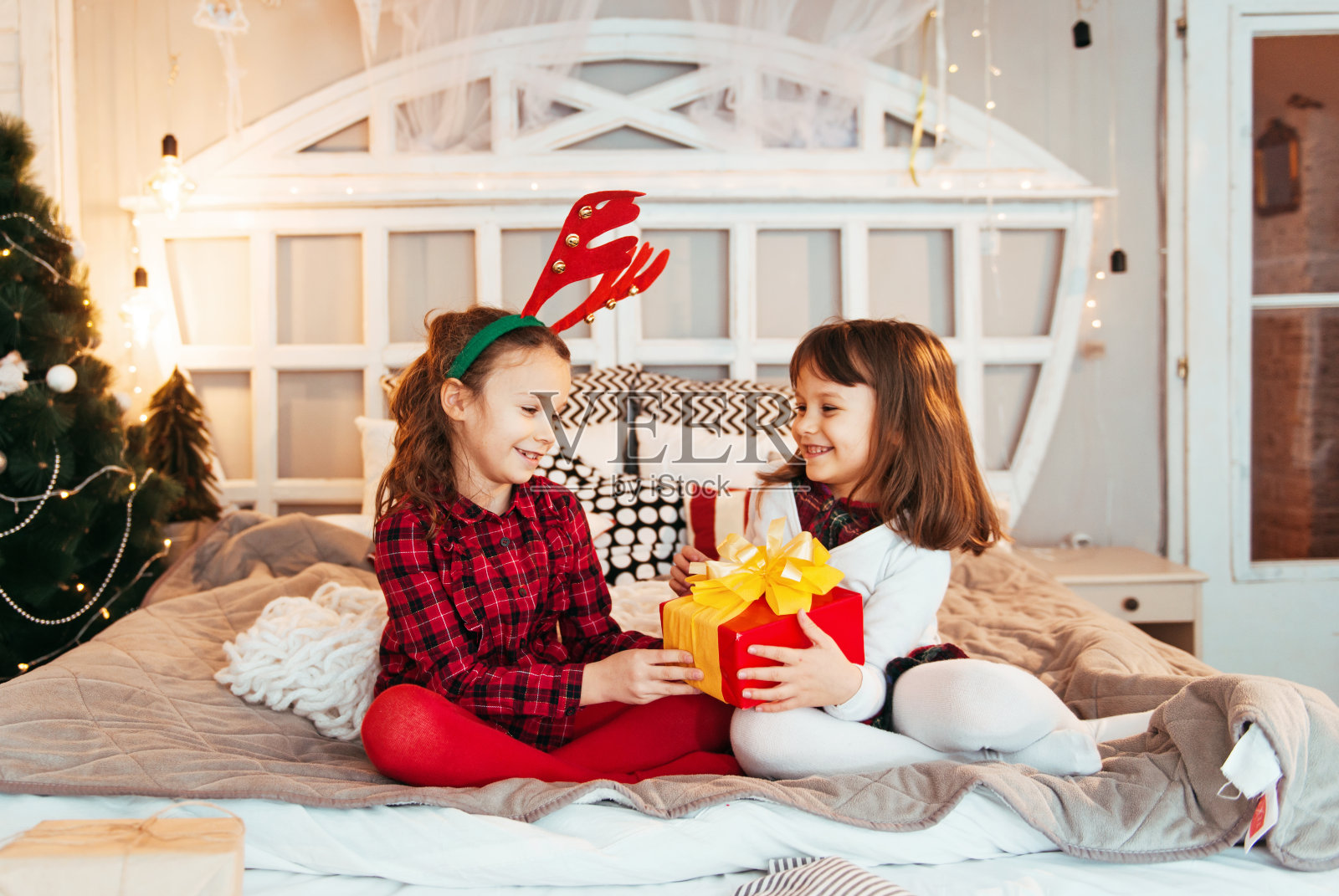 两个可爱的女孩拿着圣诞礼物，在床上玩照片摄影图片