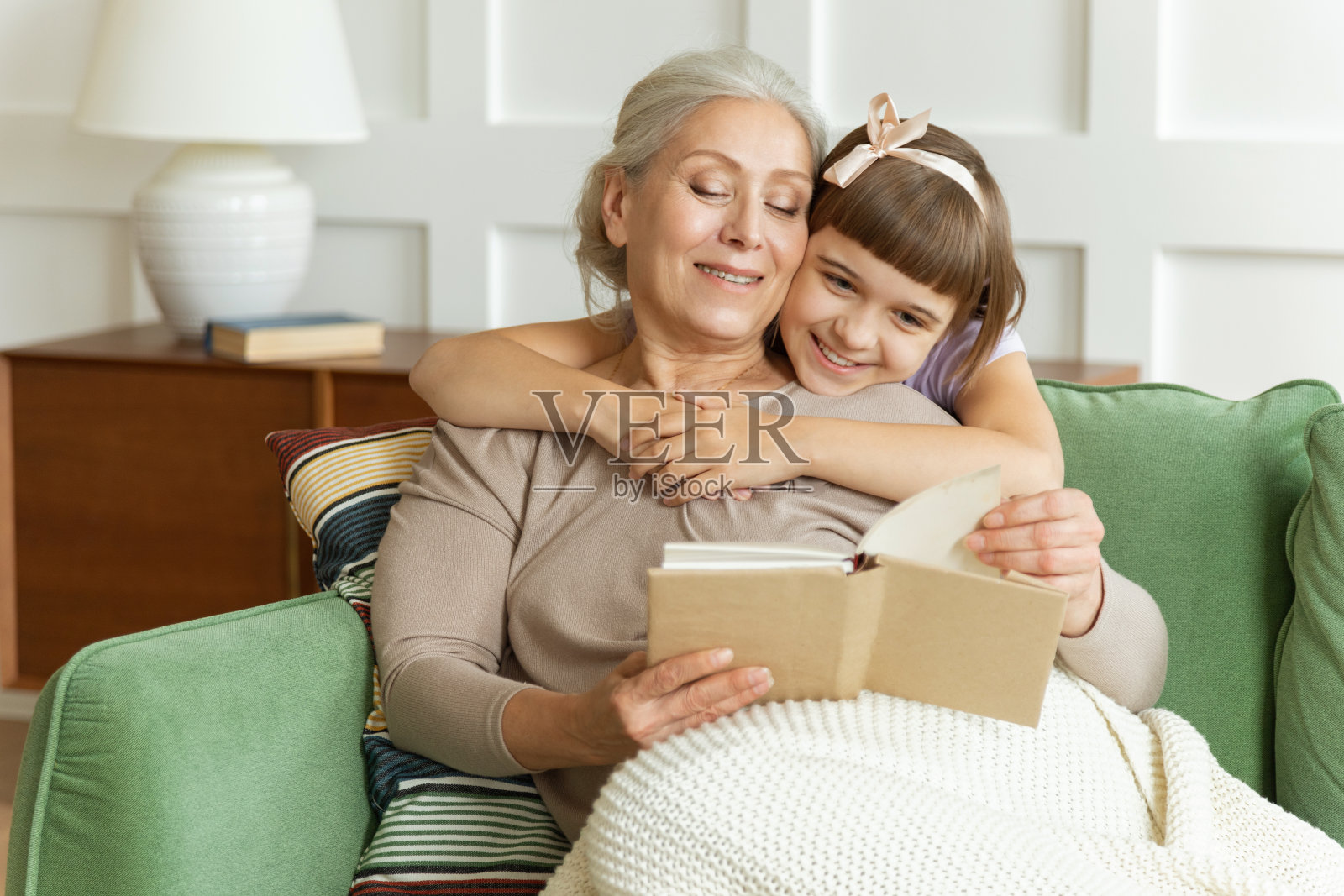 快乐漂亮的老奶奶或保姆给可爱的小女孩读模板书。照片摄影图片