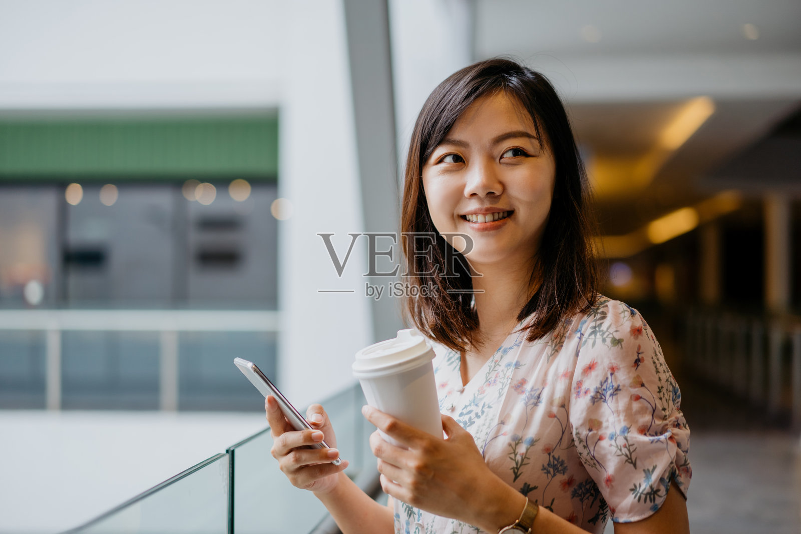 快乐的年轻亚洲女性使用智能手机和拿着纸咖啡杯照片摄影图片