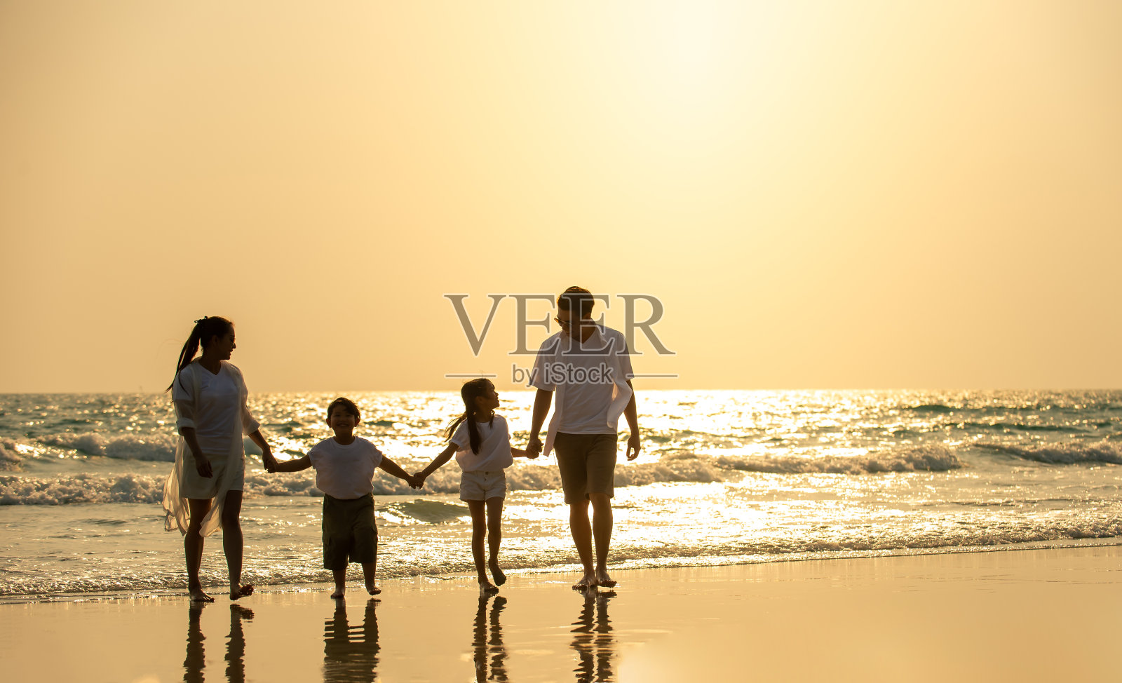 幸福的亚洲家庭父母和两个孩子的男孩和女孩手牵手一起走在海滩上在夏天的日落。父亲，母亲和孩子享受和有乐趣的户外假期假期。照片摄影图片