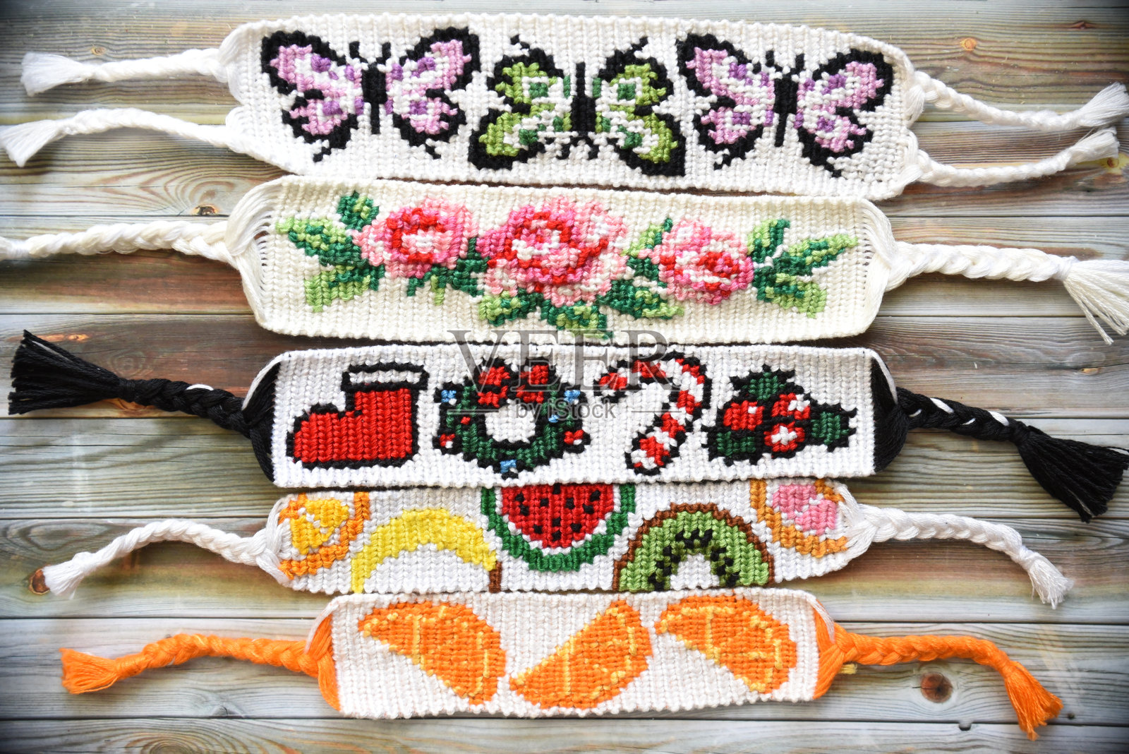 编织有阿尔法图案的五彩友谊手镯:蝴蝶、玫瑰、圣诞节、橙子和水果。木制背景上的手工线。自制的礼物的想法照片摄影图片