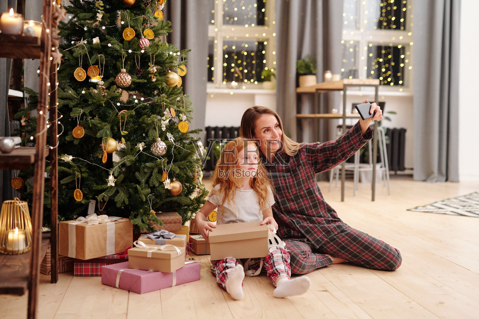 快乐的女人和可爱的小女孩穿着睡衣在圣诞树旁自拍照片摄影图片