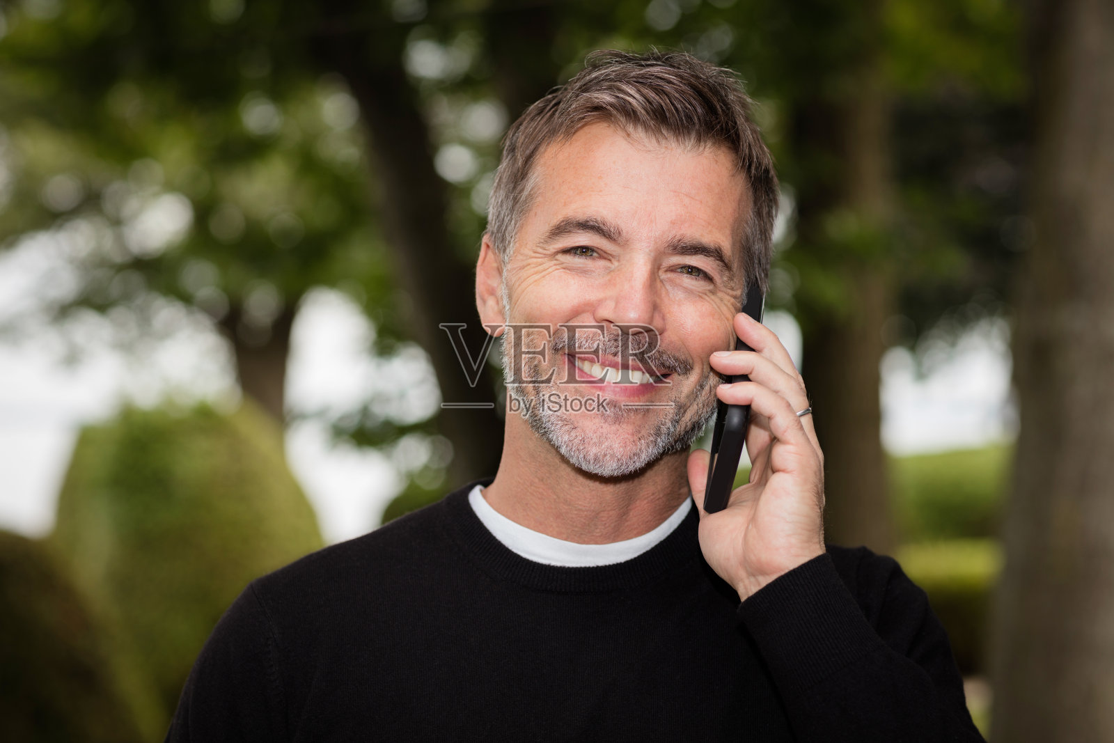 英俊成熟的快乐的男人在镜头前微笑。他在打电话。照片摄影图片