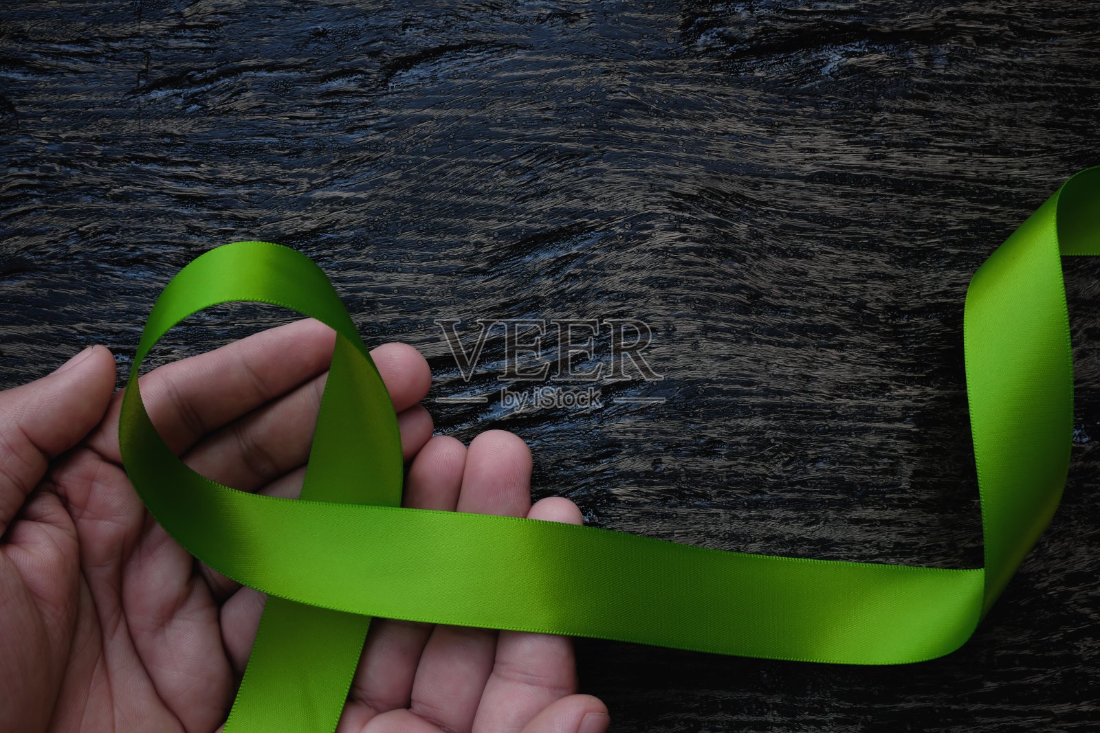 俯视图的手持有石灰绿色丝带在黑暗的背景。非霍奇金淋巴瘤、莱姆病、肌肉萎缩症和产后抑郁症意识概念照片摄影图片