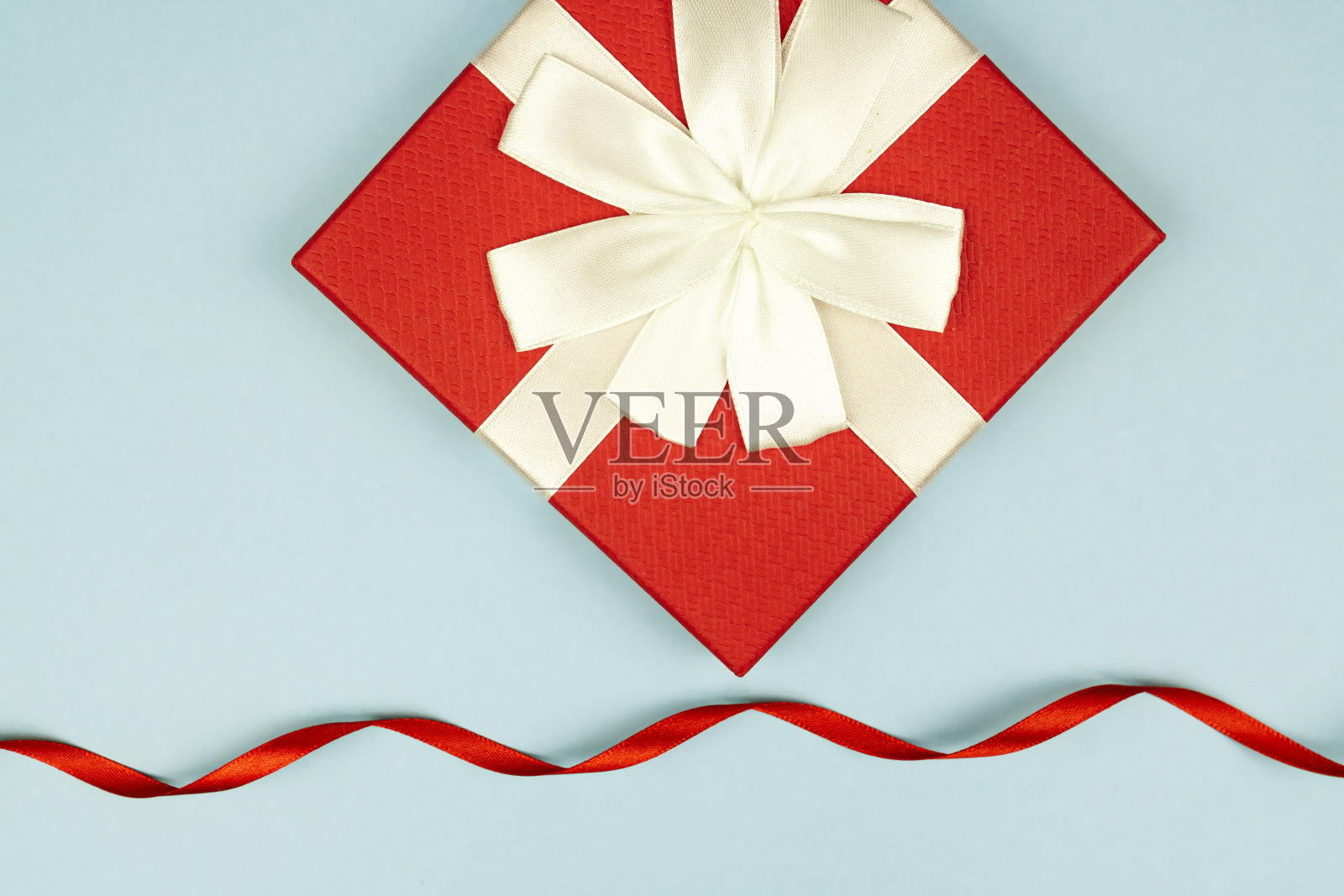 红色礼盒与缎子卷曲丝带在蓝色背景。consept Fstive假日。照片摄影图片