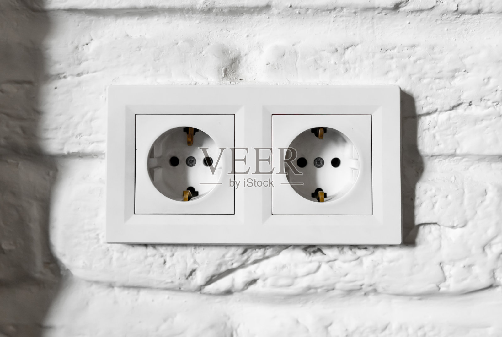 德国塑料双插座F型接地。一对空的，未插电的，欧洲白色电源插座或电源插座CEE 7，两个接地夹靠在砖墙上。照片摄影图片