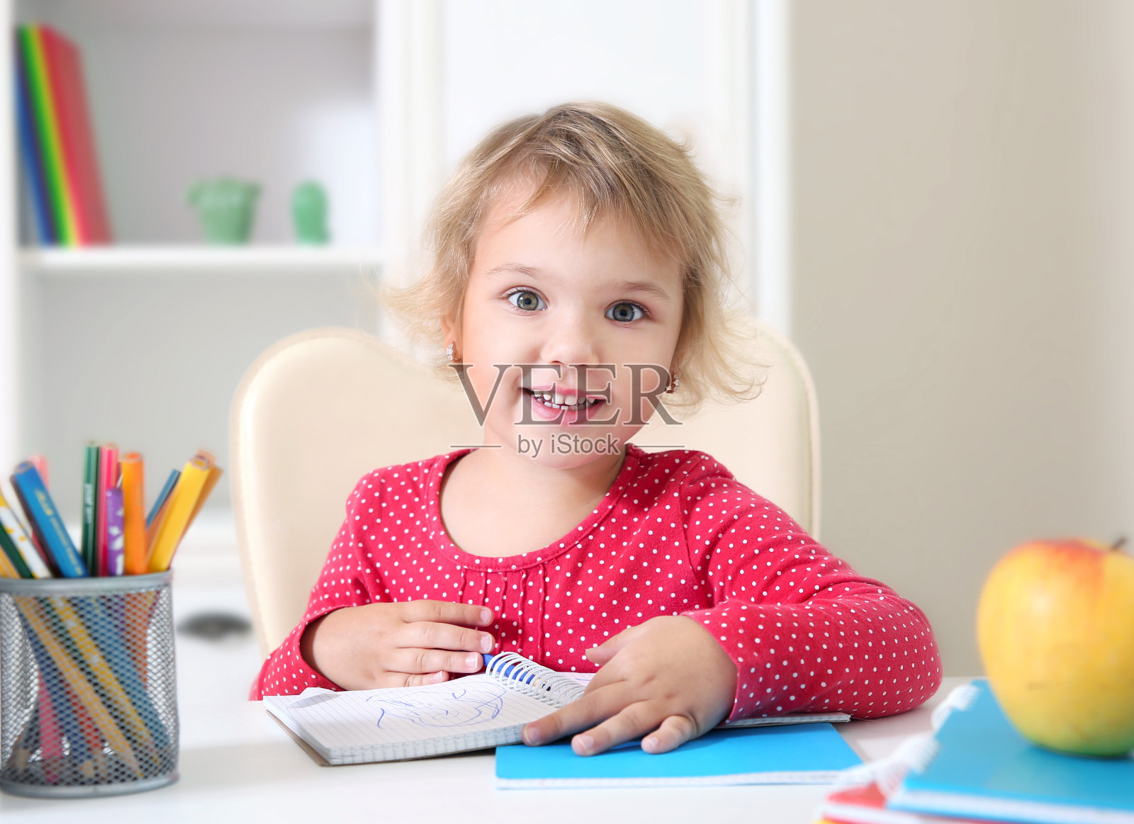 微笑的小女孩坐在桌子上，在笔记本上画画。Prescooler教育,回家学习。照片摄影图片