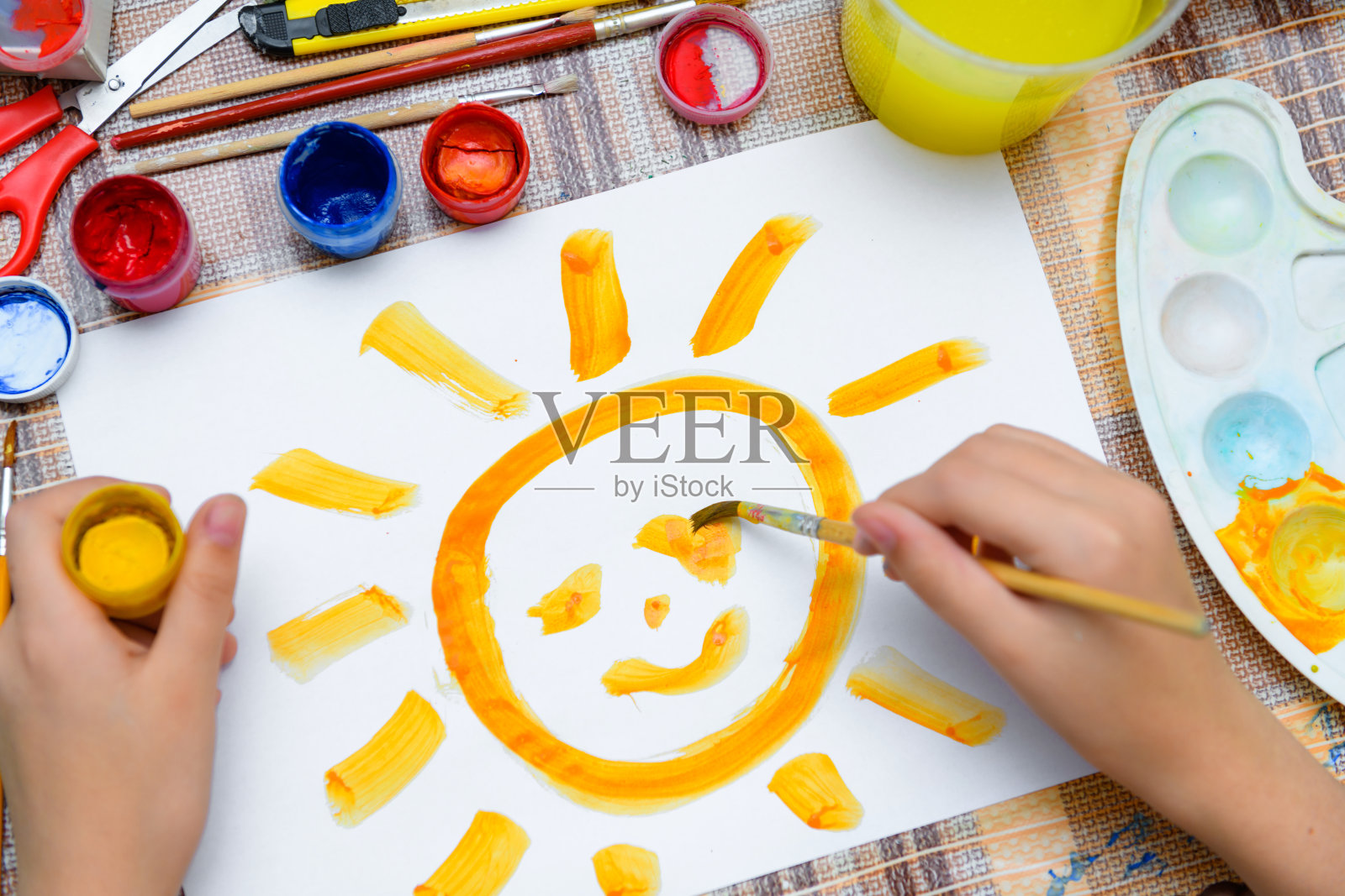 一个女孩在一张空白的白纸上画一个大大的微笑的太阳，在家里进行艺术创作，创作艺术品照片摄影图片