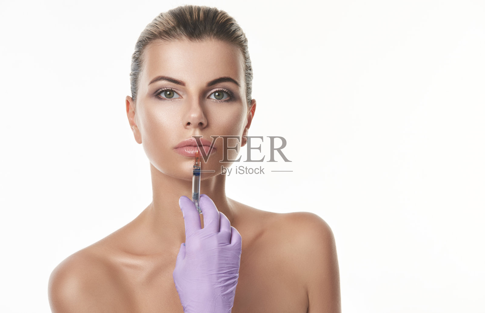 嘴唇增强的概念。漂亮的年轻女子与紫色手套拿着注射器，并使注射在嘴唇。照片摄影图片