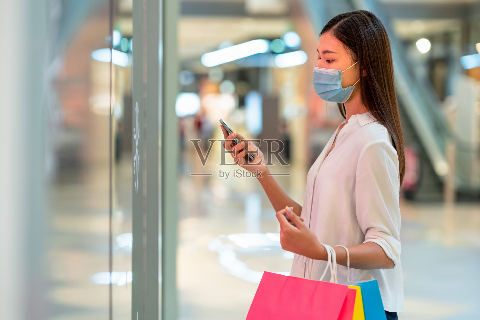 年轻美丽的女人走在购物中心微笑。用她的智能手机和朋友聊天。购物消费的概念照片摄影图片