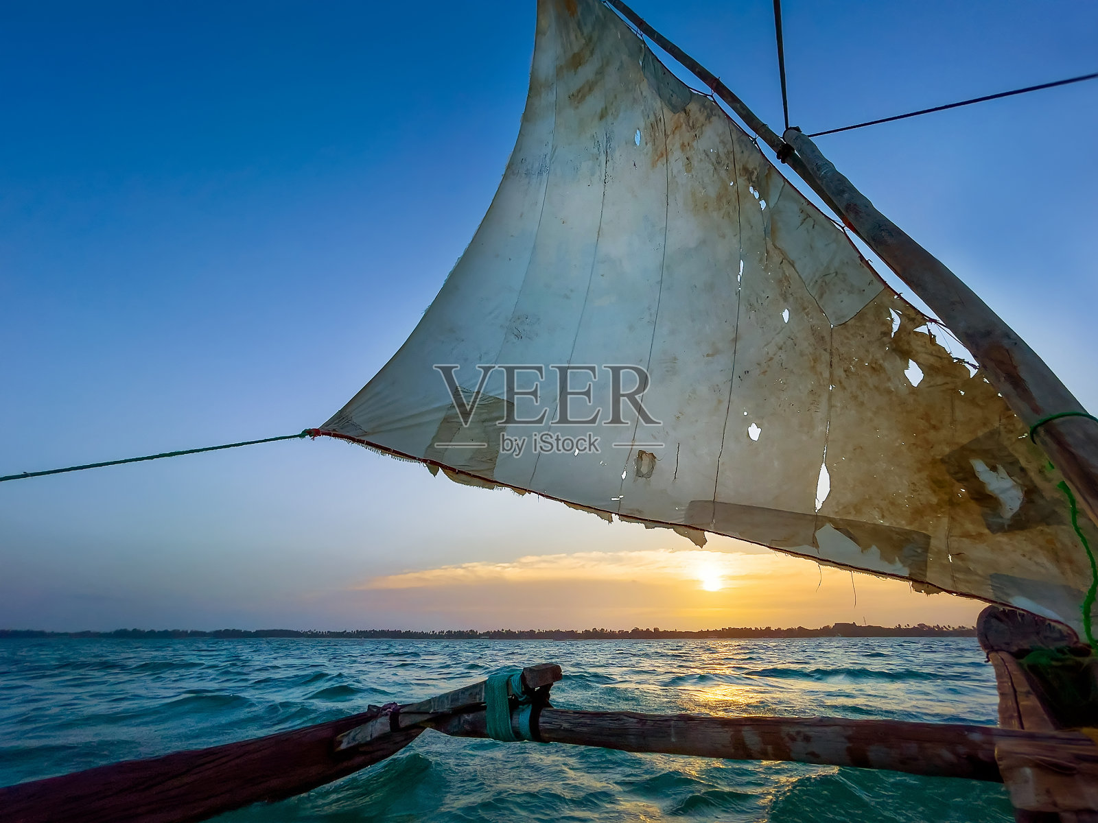 在美丽的夕阳中，坦桑尼亚桑给巴尔岛附近开阔的印度洋上，古老的传统海事传统船只三角帆在撕裂的帆下航行。旅游和独特的地方文化观念。照片摄影图片