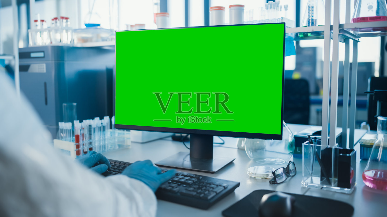 先进实验室:微生物科学家在键盘上打字与绿色键盘屏幕计算机开发疫苗，药物和抗生素。高科技实验室架子上有试管，药瓶照片摄影图片