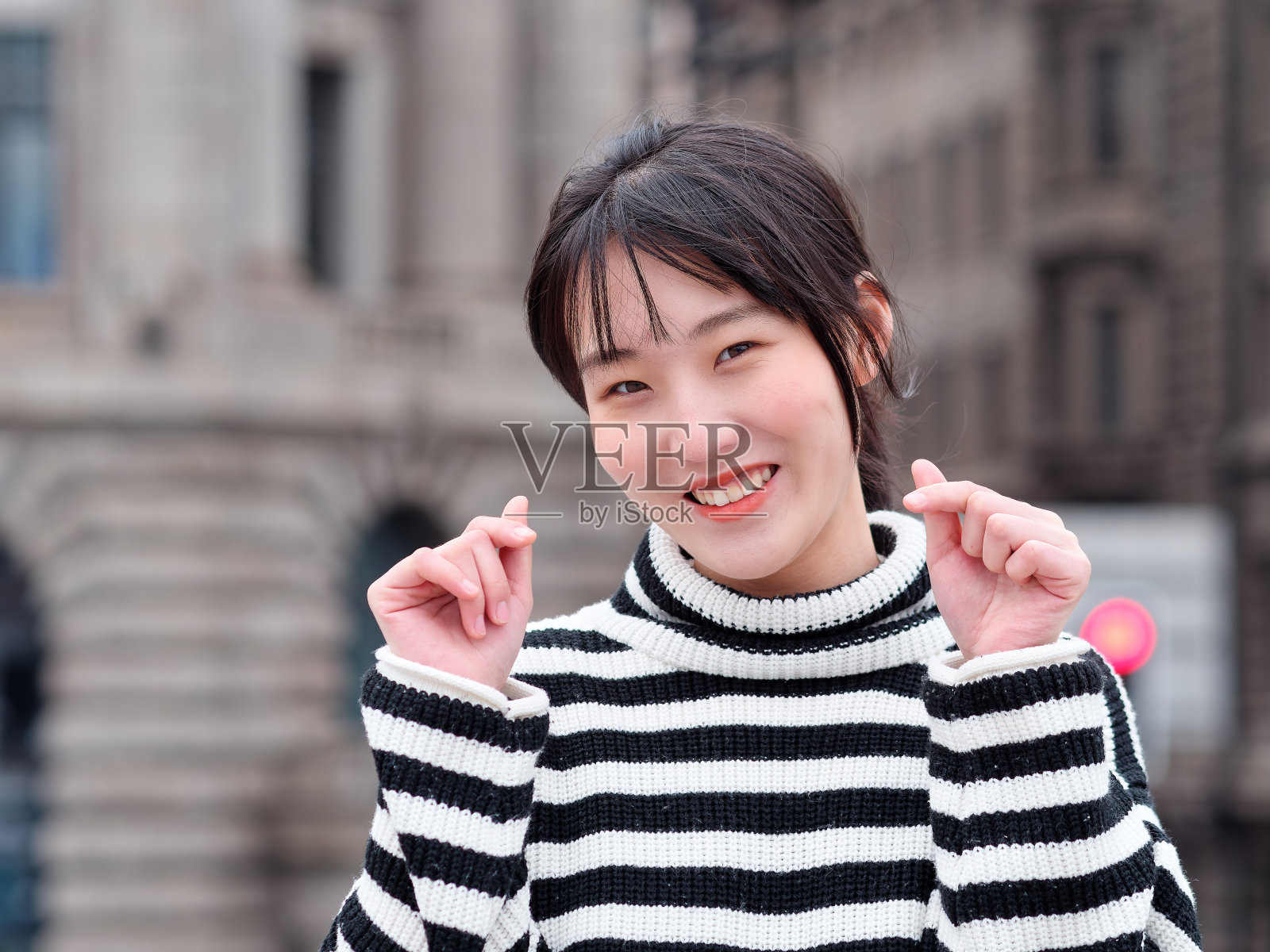 年轻的中国女人在镜头前微笑着用爱你的手势，快乐的女孩与城市建筑背景在上海的肖像。照片摄影图片