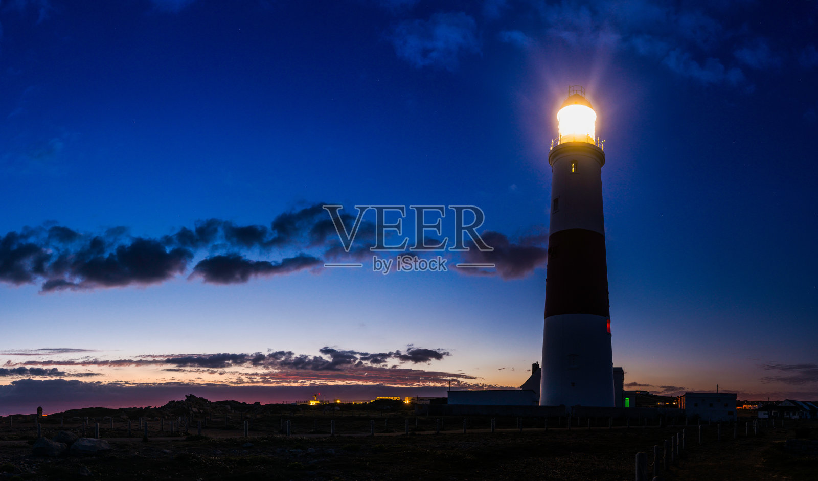 灯塔从海洋的悬崖顶上向蓝色的黄昏天空发光照片摄影图片