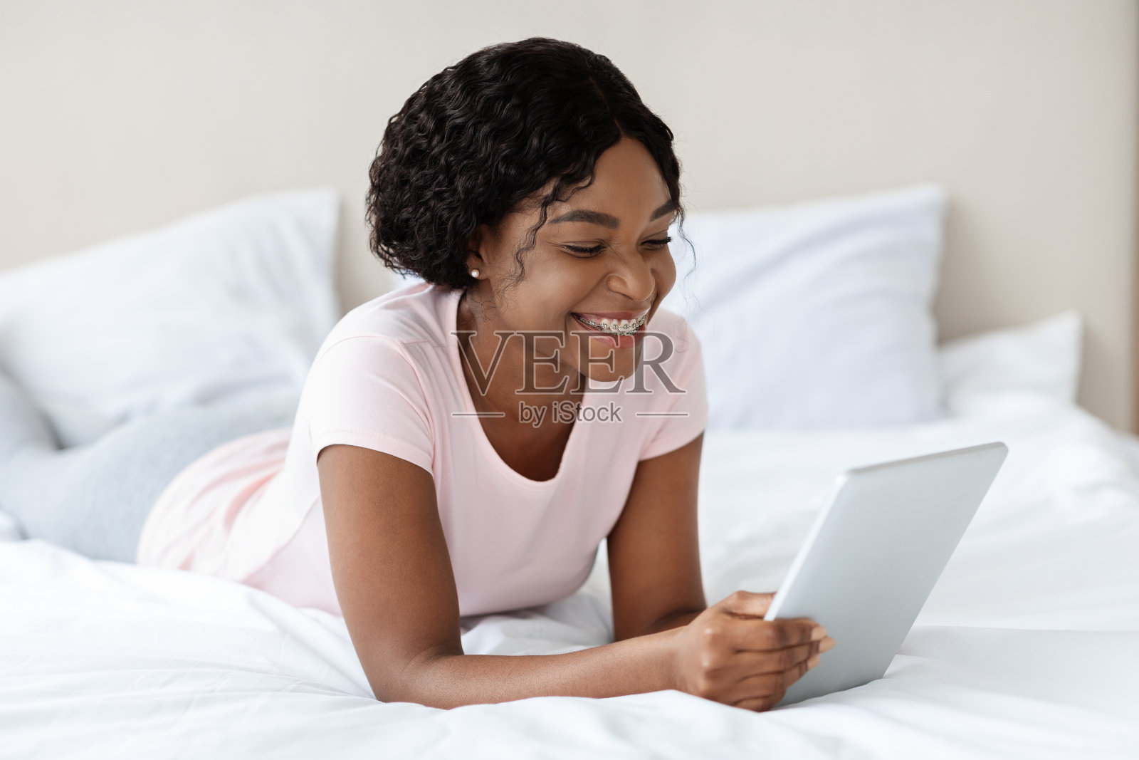 微笑的黑人妇女躺在床上，用着数字平板电脑照片摄影图片