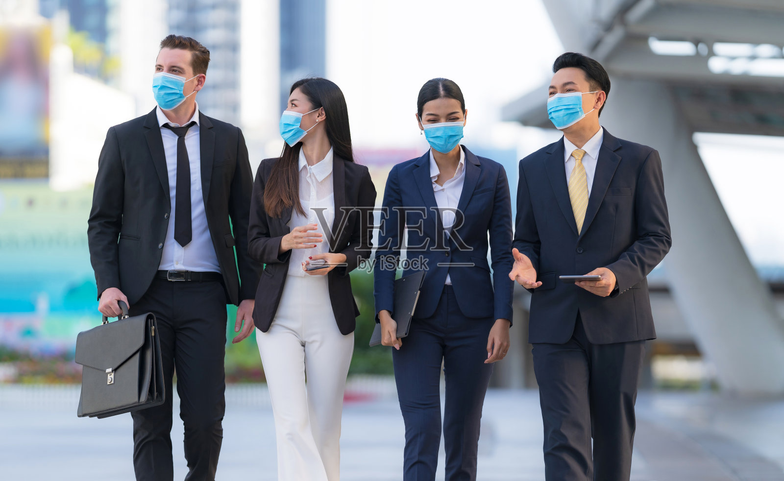 四名戴着手术安全口罩的商人走在现代化的办公室前照片摄影图片