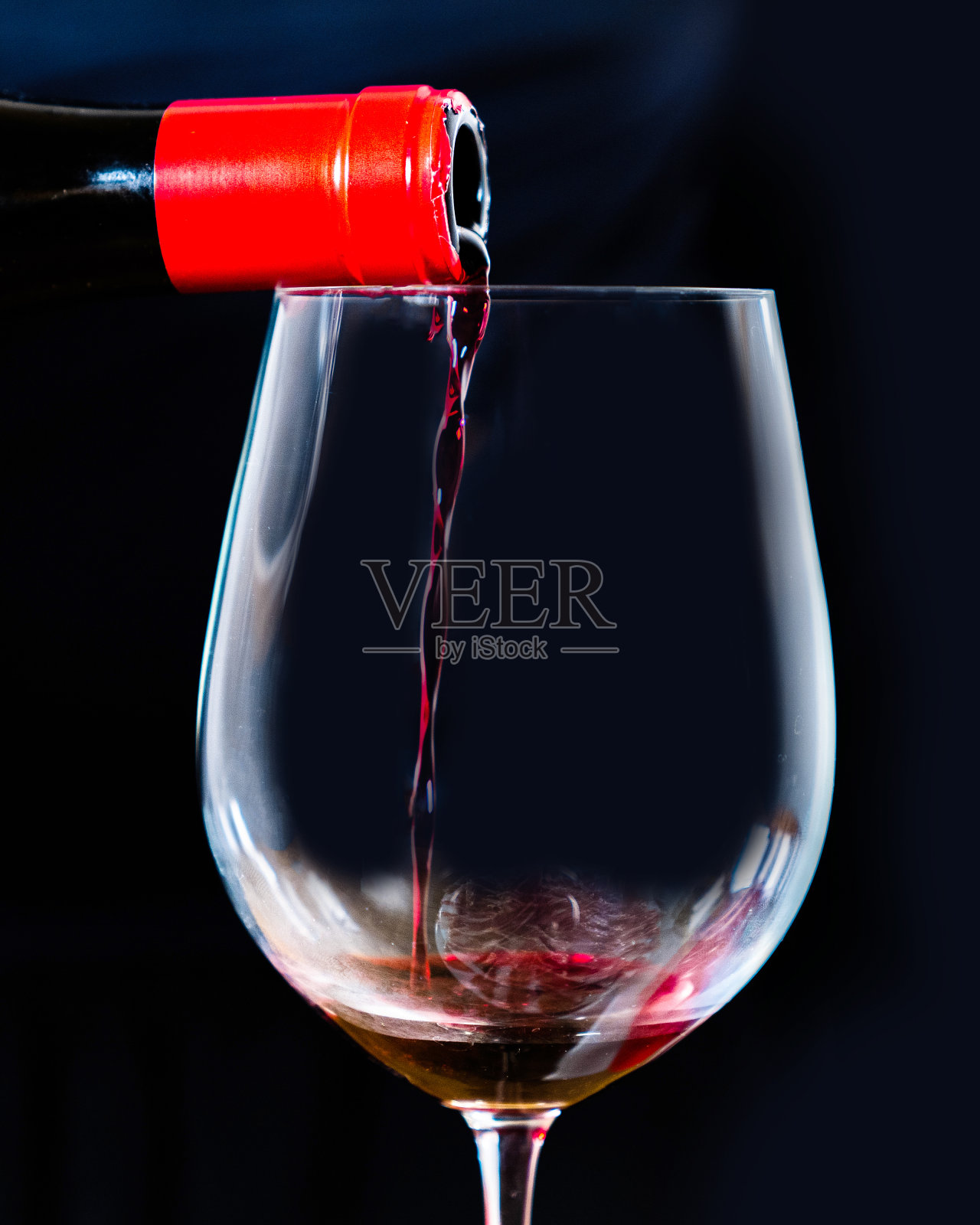 侍酒师服务西班牙黑葡萄酒在一个优雅的水晶高脚杯与黑色的背景。将红酒从瓶中倒入黑色酒杯中。照片摄影图片