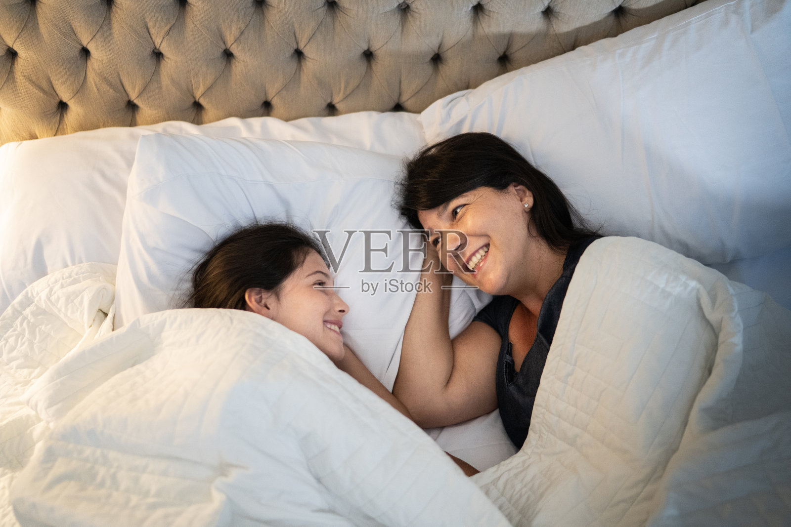 快乐的女孩躺在床上陪妈妈在家照片摄影图片