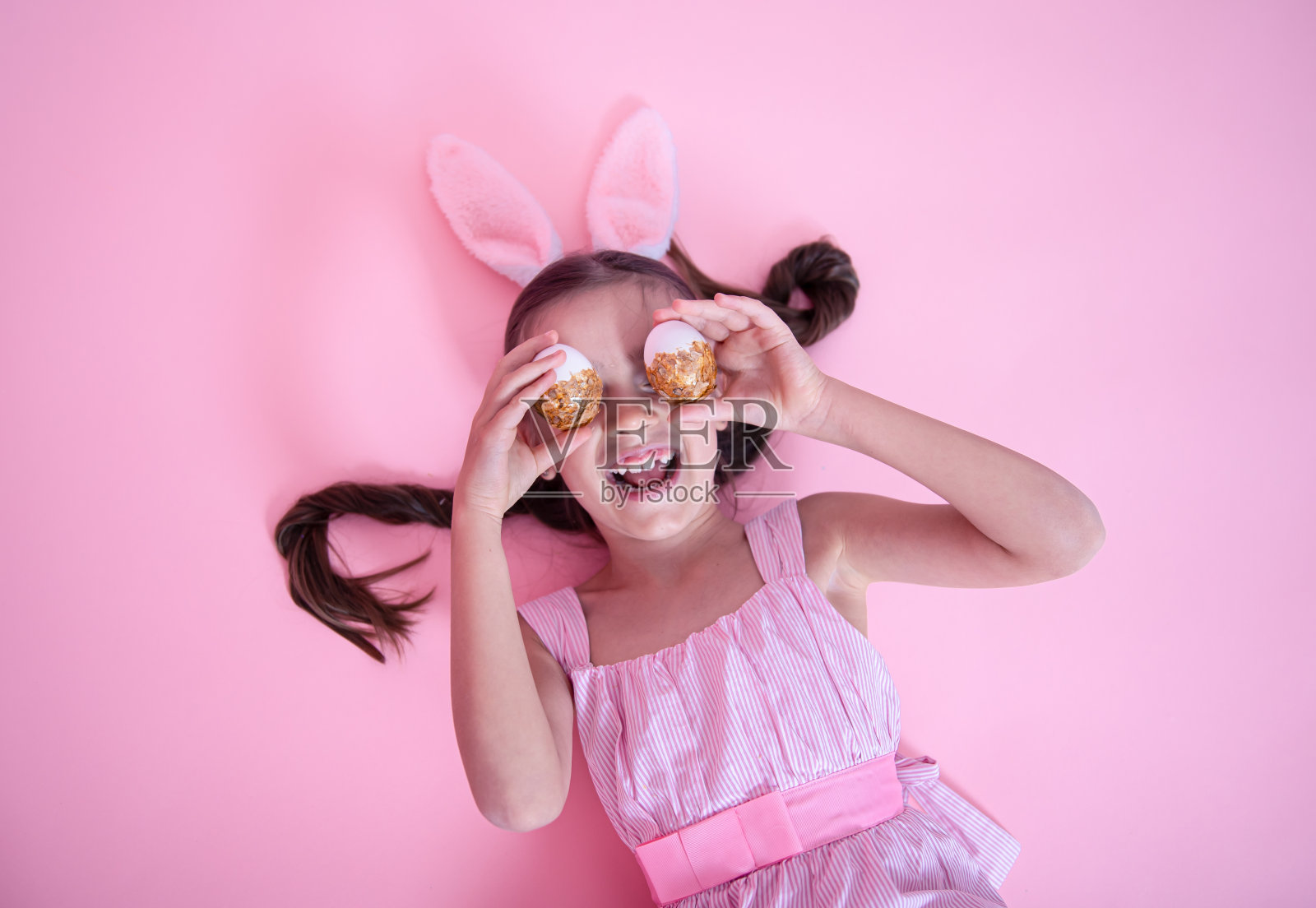 快乐的小女孩，穿着复活节兔子耳朵和连衣裙，摆着复活节彩蛋的姿势。照片摄影图片