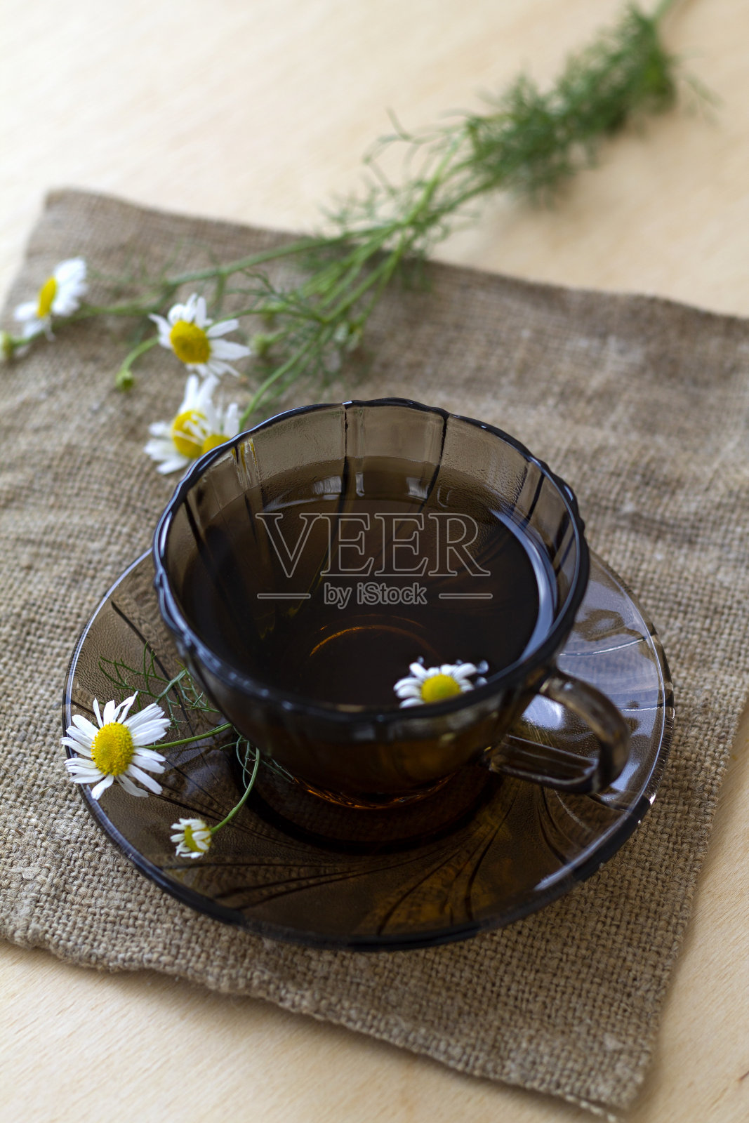 深色玻璃杯里放着一杯凉茶和甘菊茶，放在一张有复印空间的轻木桌上。杯茶，花束鲜花和绿色的叶子在黄色的背景。健康的生活方式。照片摄影图片