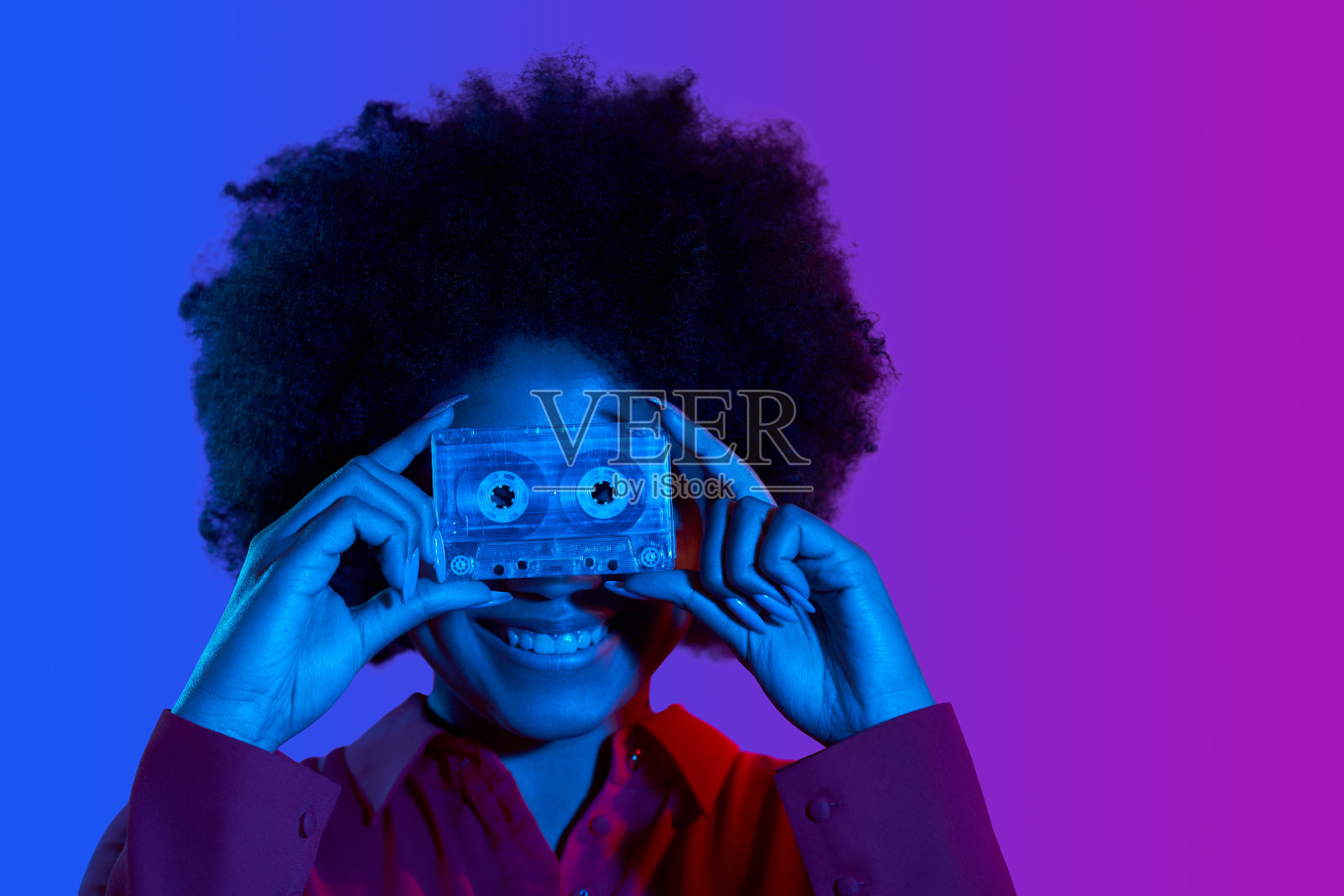 滑稽的非洲妇女肖像拿着复古音乐磁带在前面，双色霓虹灯照片摄影图片