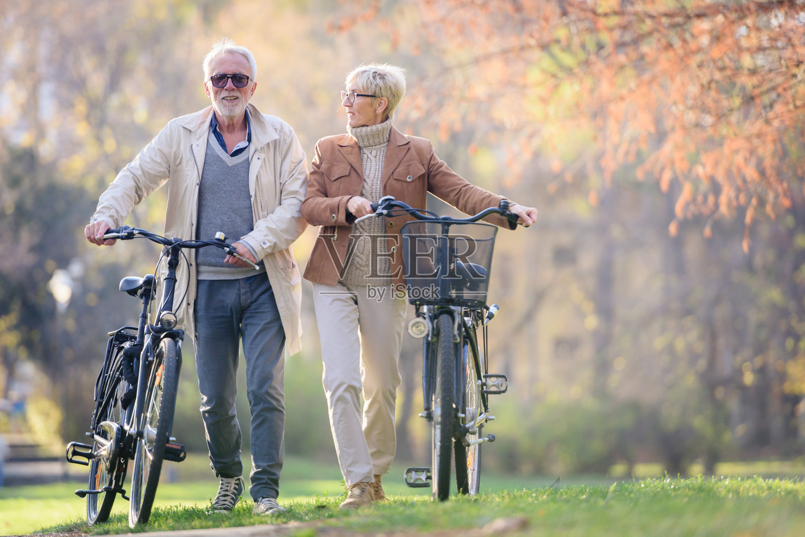 活泼愉快的老年夫妇骑着自行车一起在公园里散步。适合老年人的完美活动。照片摄影图片