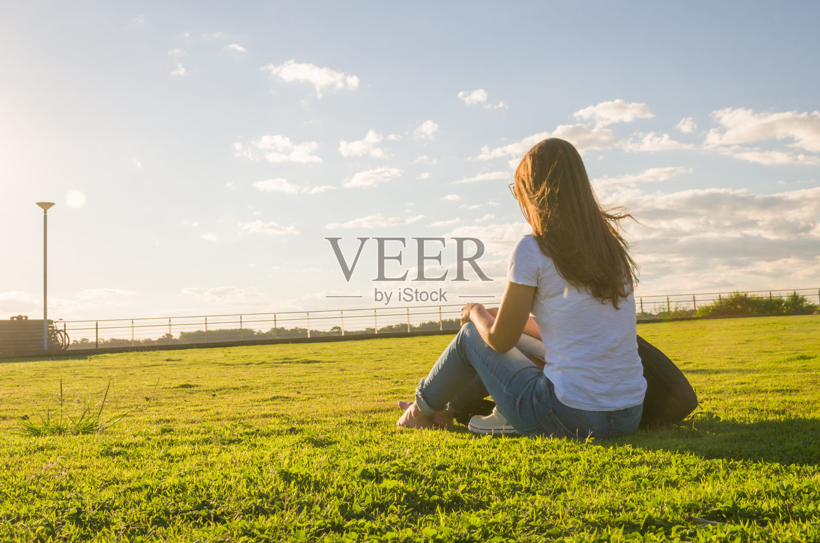 在SARS CoV-2大流行季节(冠状病毒)，年轻女子戴着防护口罩坐在草地上)照片摄影图片