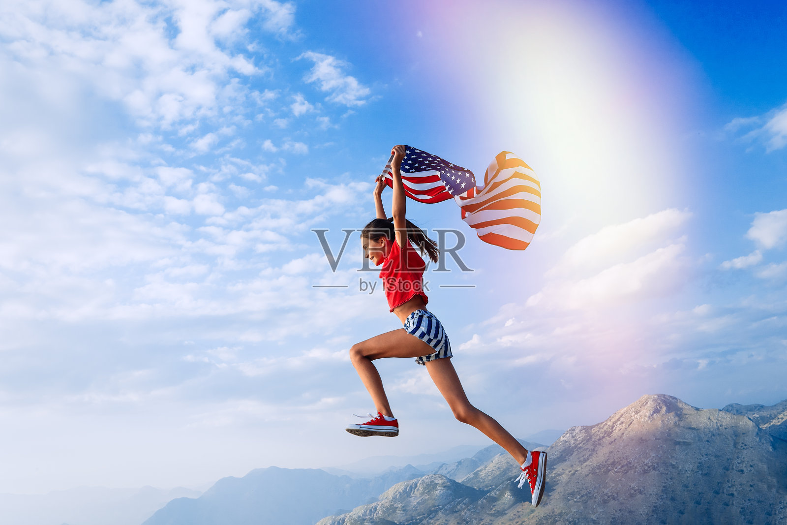 一个十几岁的女孩在山顶上跳着，她的肩膀上有一面美国国旗照片摄影图片