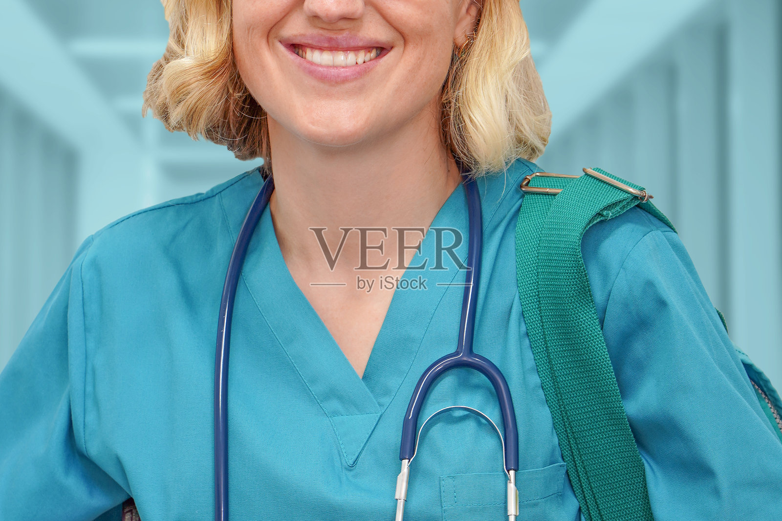 戴眼镜、身穿蓝色制服、拿着书和包的实习外科医生，背景是诊所模糊的走廊照片摄影图片