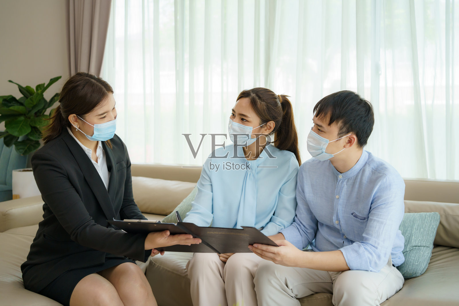 亚洲女性保险经纪人正在亚洲夫妇家中客厅向他们提供COVID-19健康保险的详细信息。照片摄影图片