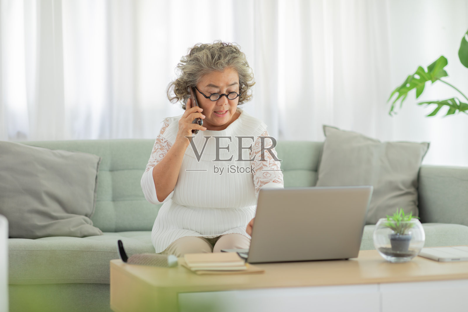 一名白发苍苍的亚洲老年妇女通过手机与客服沟通，以寻求解决电脑问题或人为失误的解决方案照片摄影图片